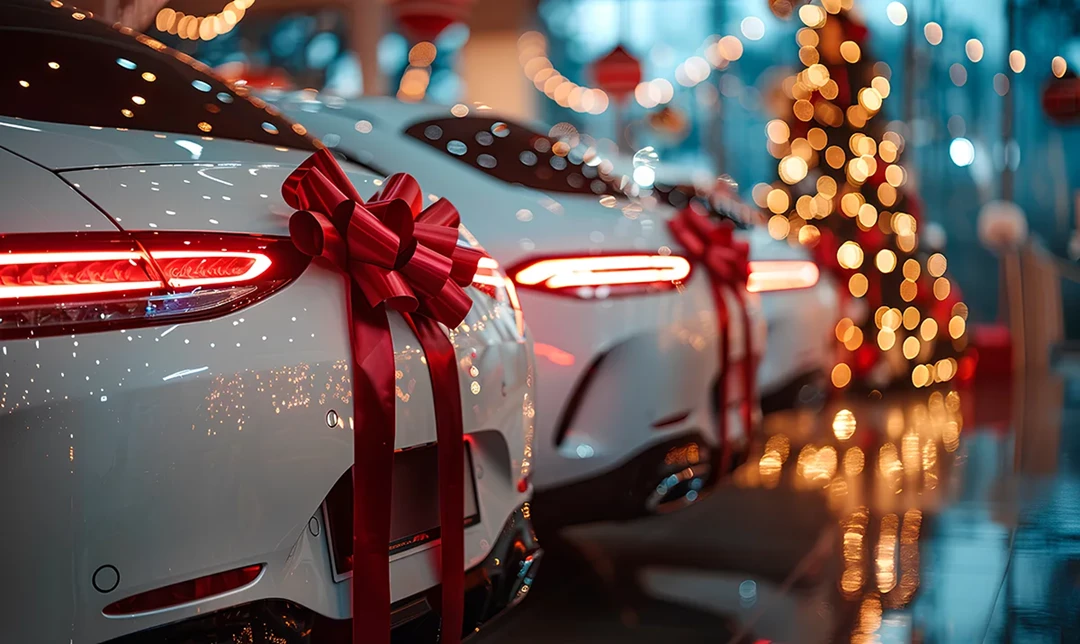 Cars in showroom at Christmas with a red ribbon on them and a lit christmas tree in the background