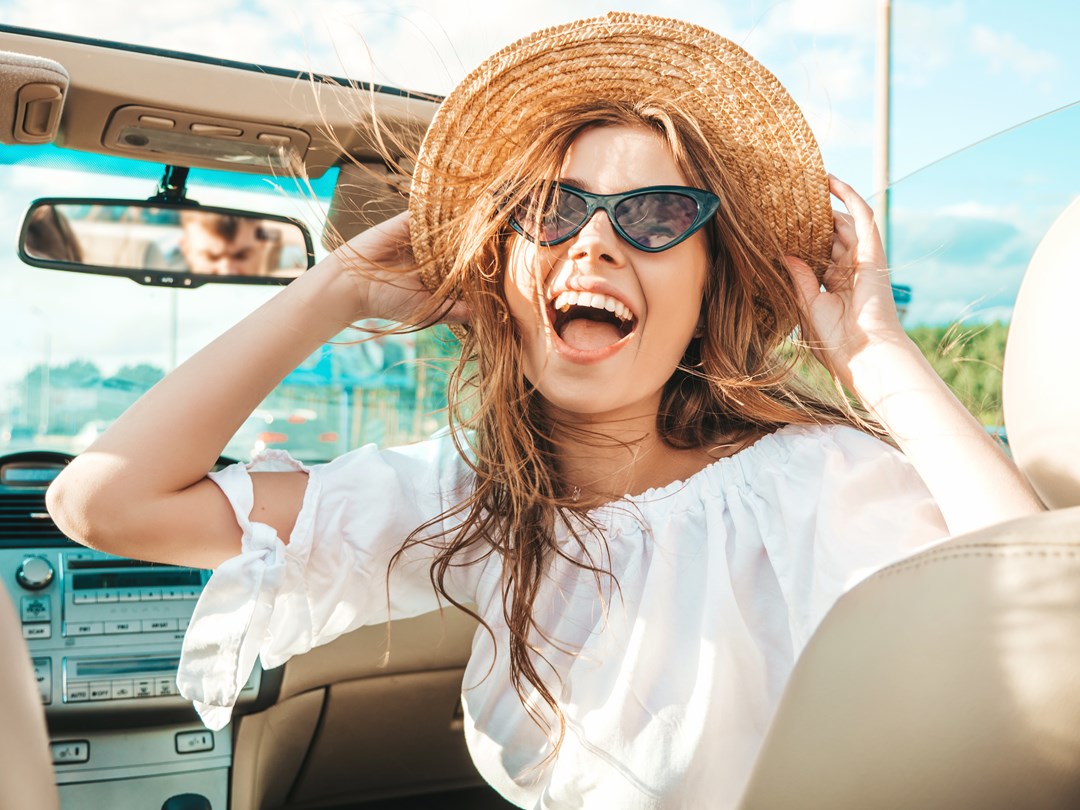 Happy young woman in a straw hat and sunglasses in a car on a sunny day