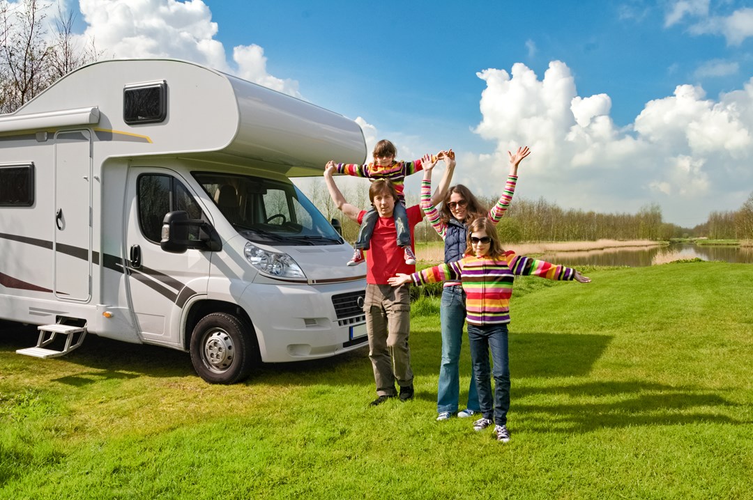 Happy family in colourful clothes in a field, beside their campervan