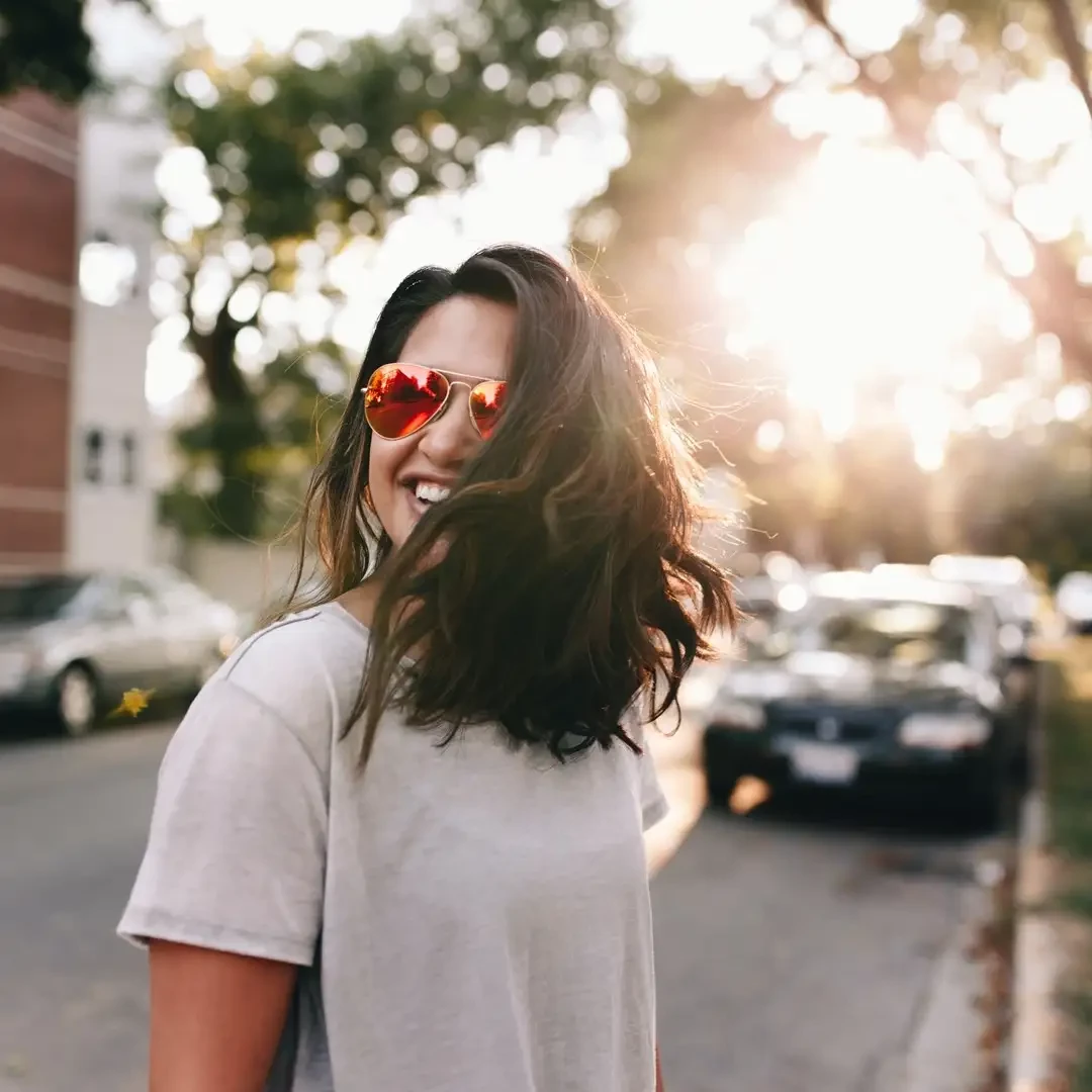 Woman in the street with orange shades and smiling.