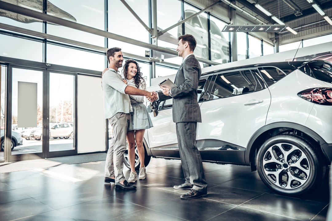 Couple shaking hands with a car dealer next to a new car