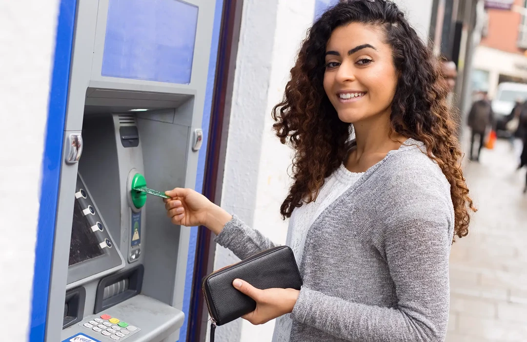 Young woman withdrawing cash from ATM machine in the street