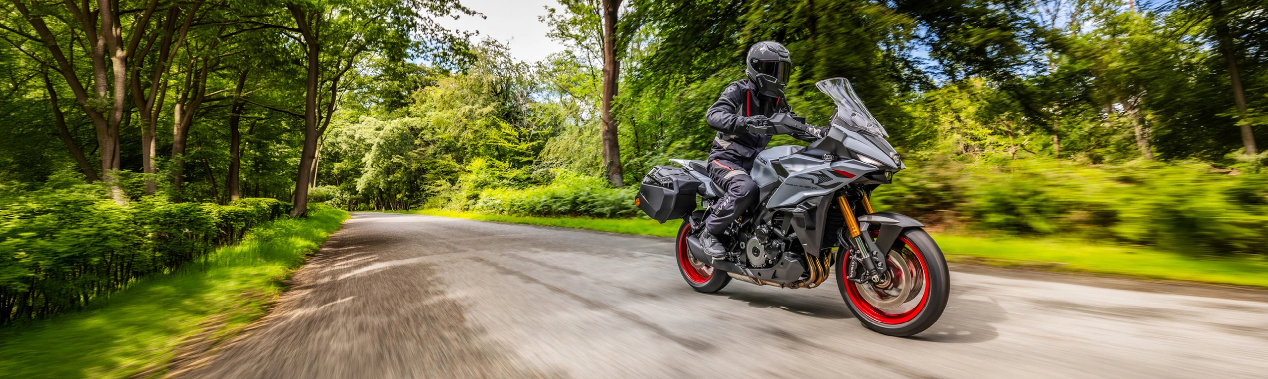 Suzuki GSX-S1000GX+ riding along a country road lined by trees.