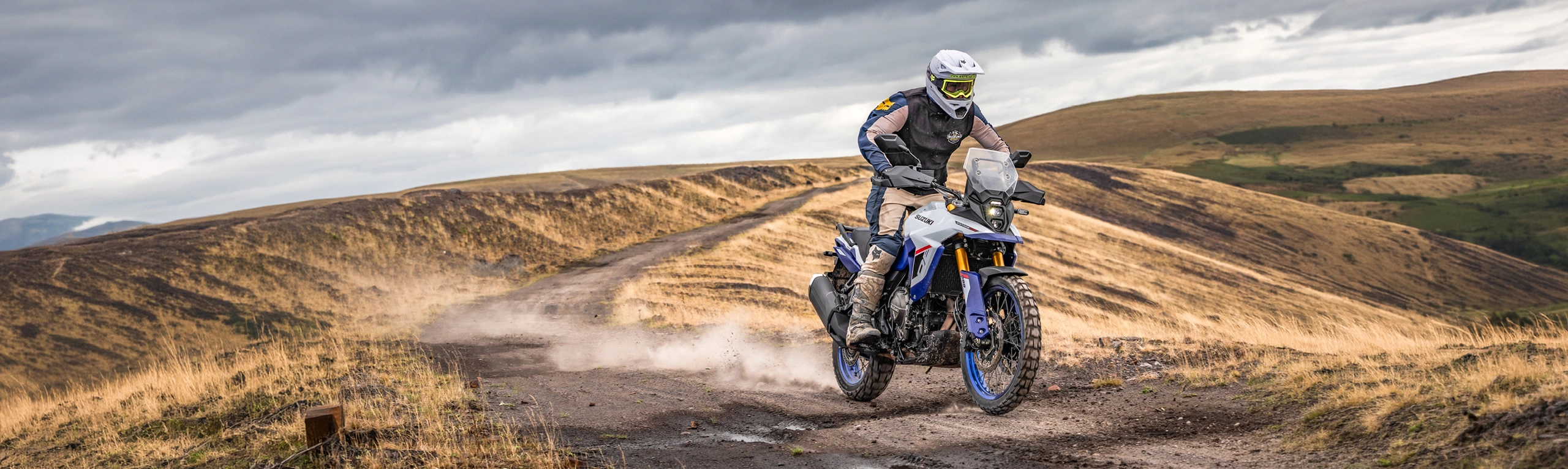 Suzuki V-Strom 800DE pushing on along a dirt track with mountains behind