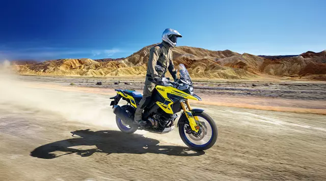 Suzuki V-Strom 1050DE riding through sand dunes, rider standing up on the pegs.