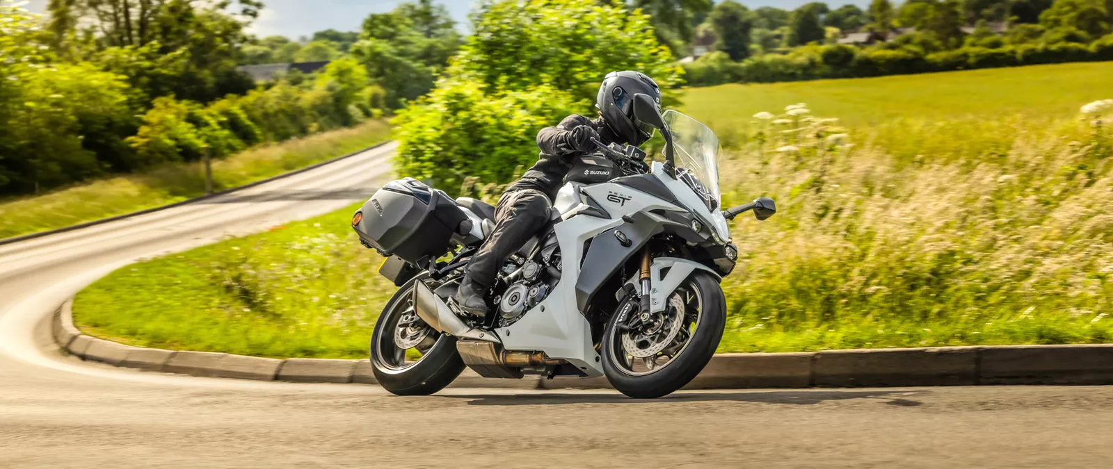 Suzuki GSX-S1000GT+ leaning into a corner on a country road.