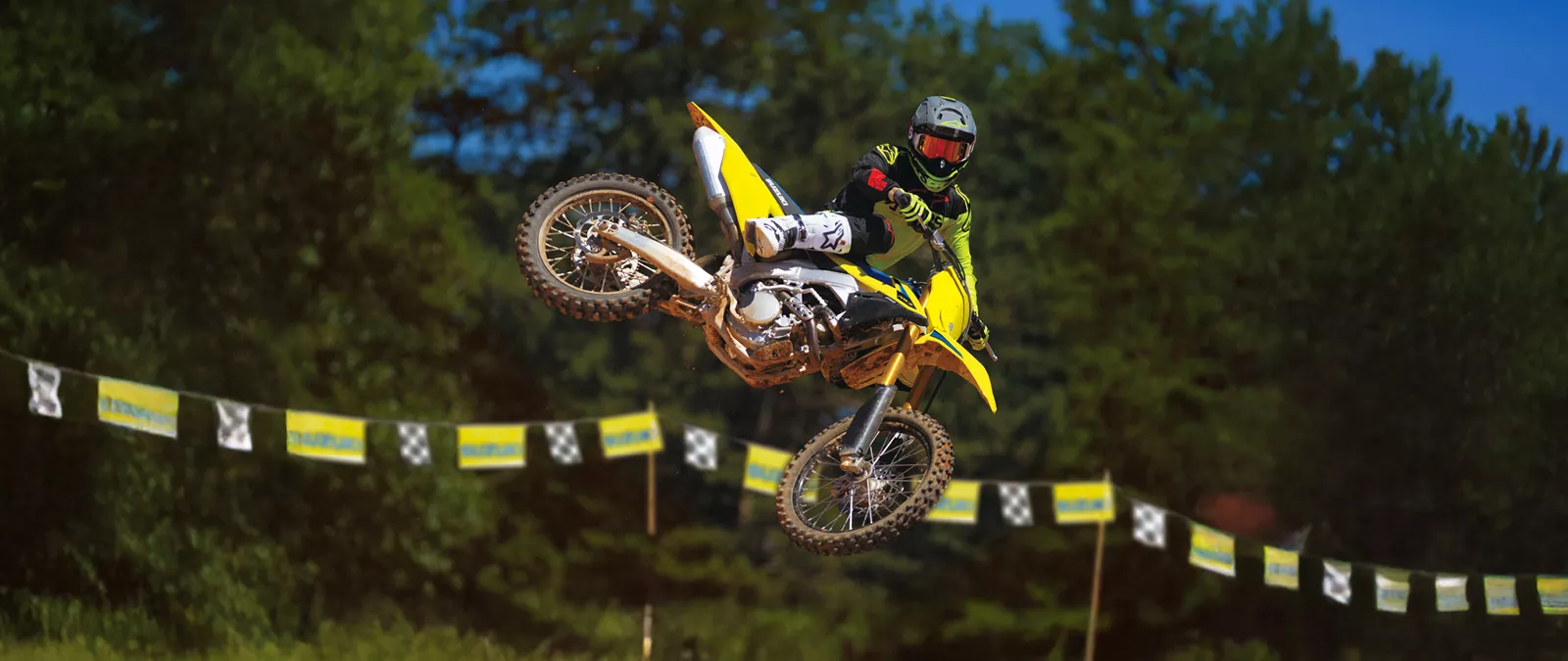 Suzuki RM-Z250 whip over a jump with trees in the background