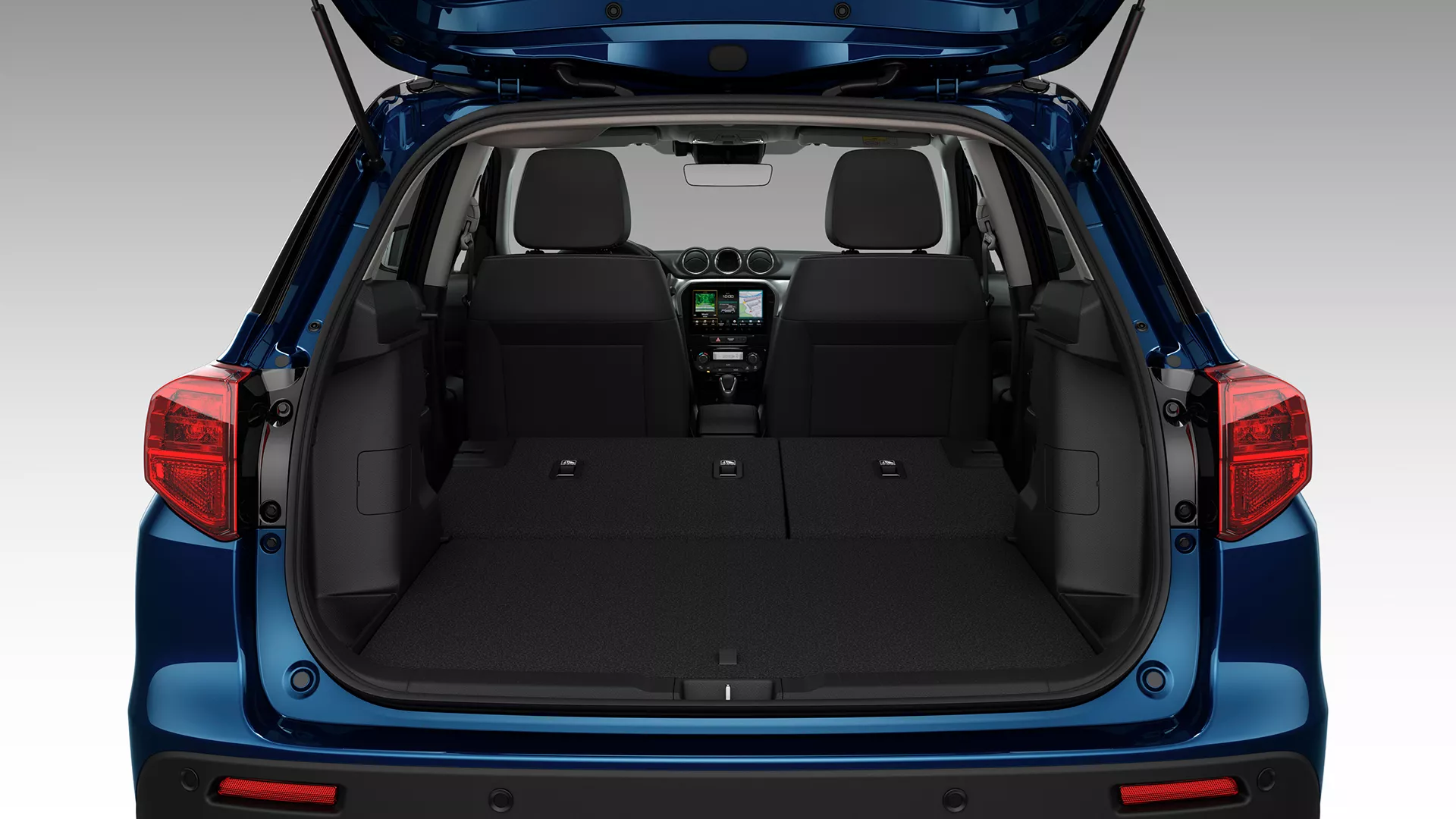 Rear view of the Suzuki Vitara with the tailgate open, showcasing the spacious boot area and flat-folding rear seats for expanded cargo capacity.