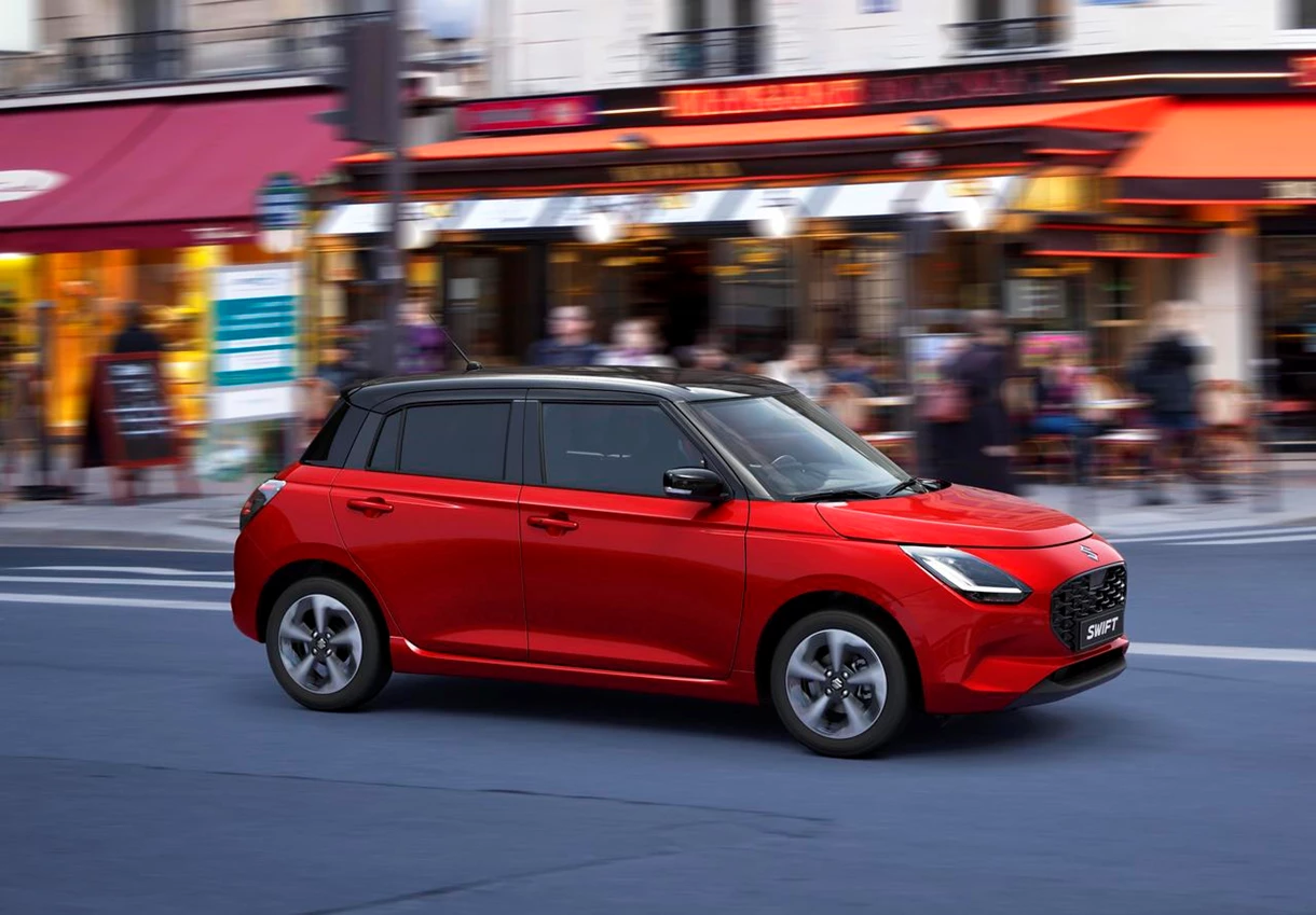 New red Suzuki Swift driving in busy city
