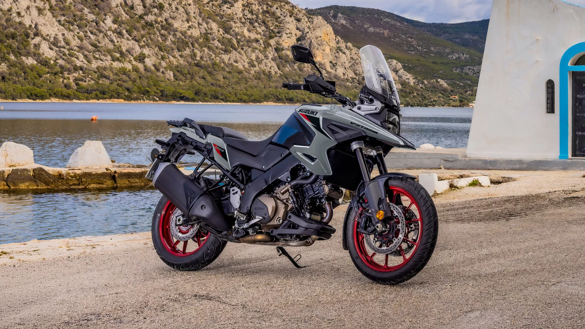 Suzuki V-Strom 1050RE grey, static beside a church with a river and mountain backdrop