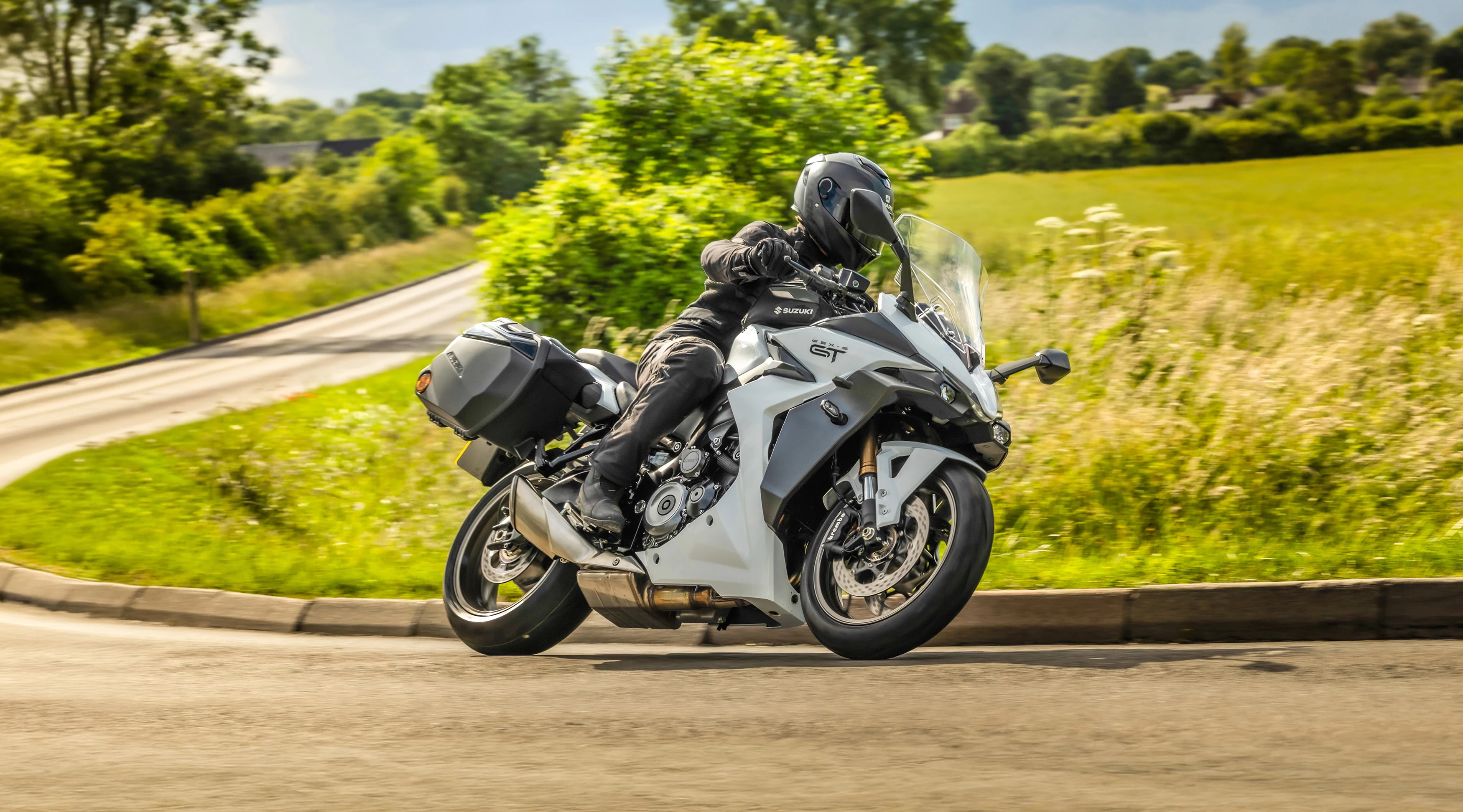 Suzuki GSX-S1000GT+ turning hard into a corner with a field behind.