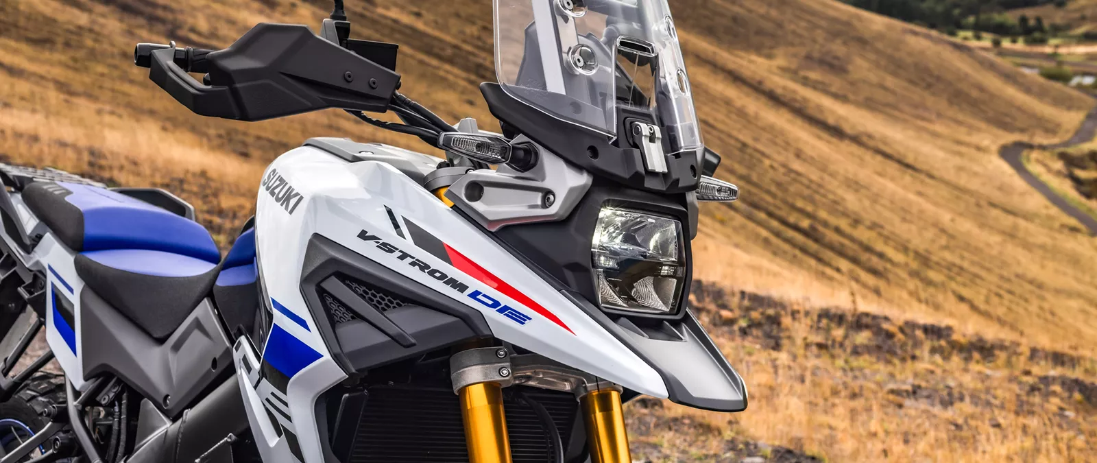 Suzuki V-Strom 1050DE white front headlight and beak close up, with a mountain backdrop