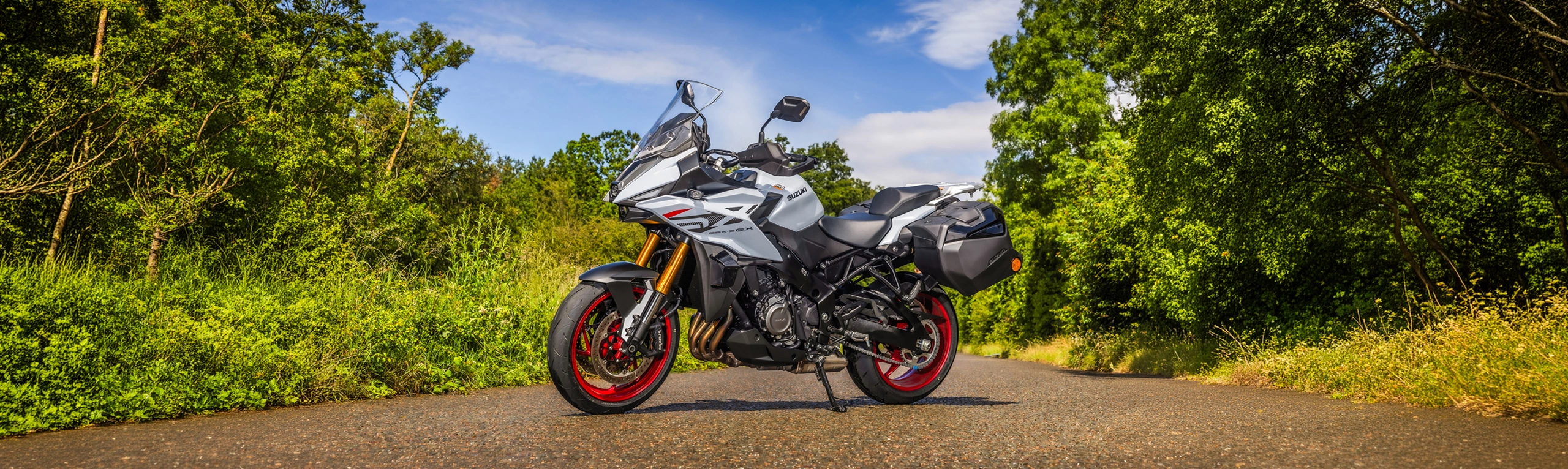 Suzuki GSX-S1000GX+ parked on side stand on a quiet country road, with blue skies