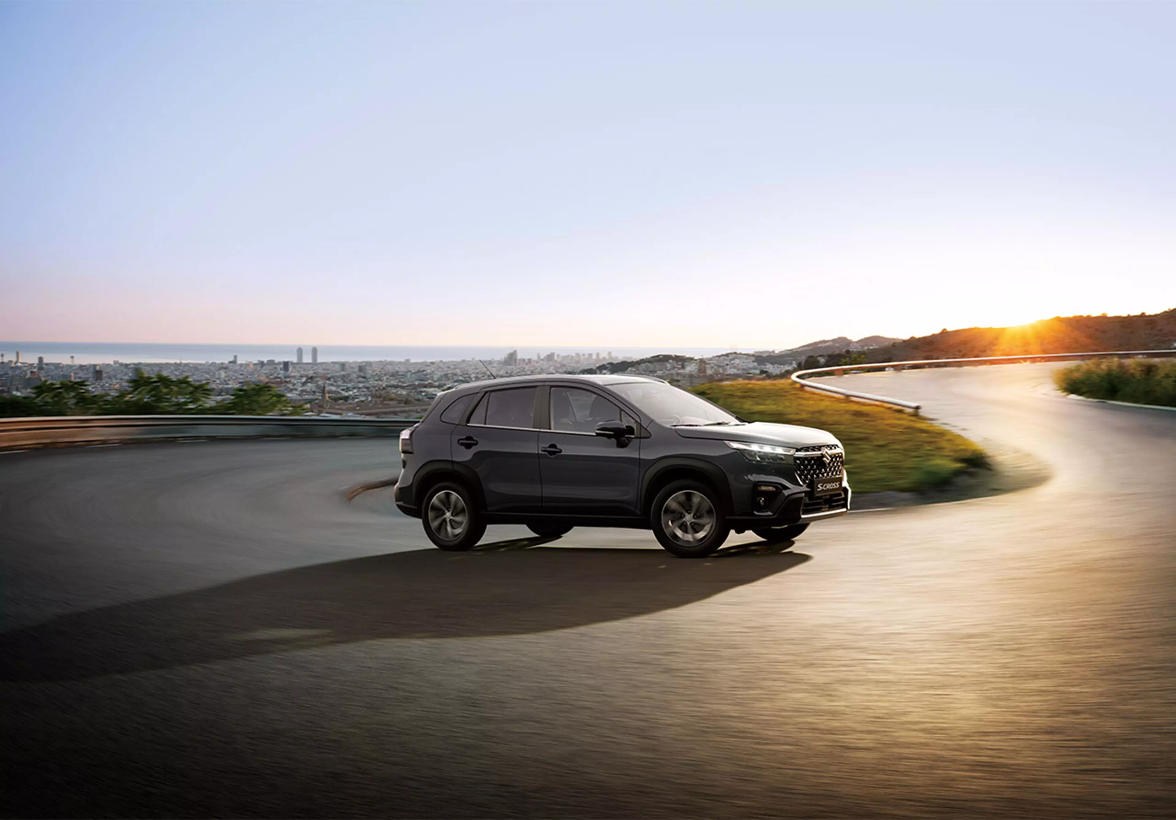 Side view of a grey Suzuki S-Cross on an asphalt road at sunset.