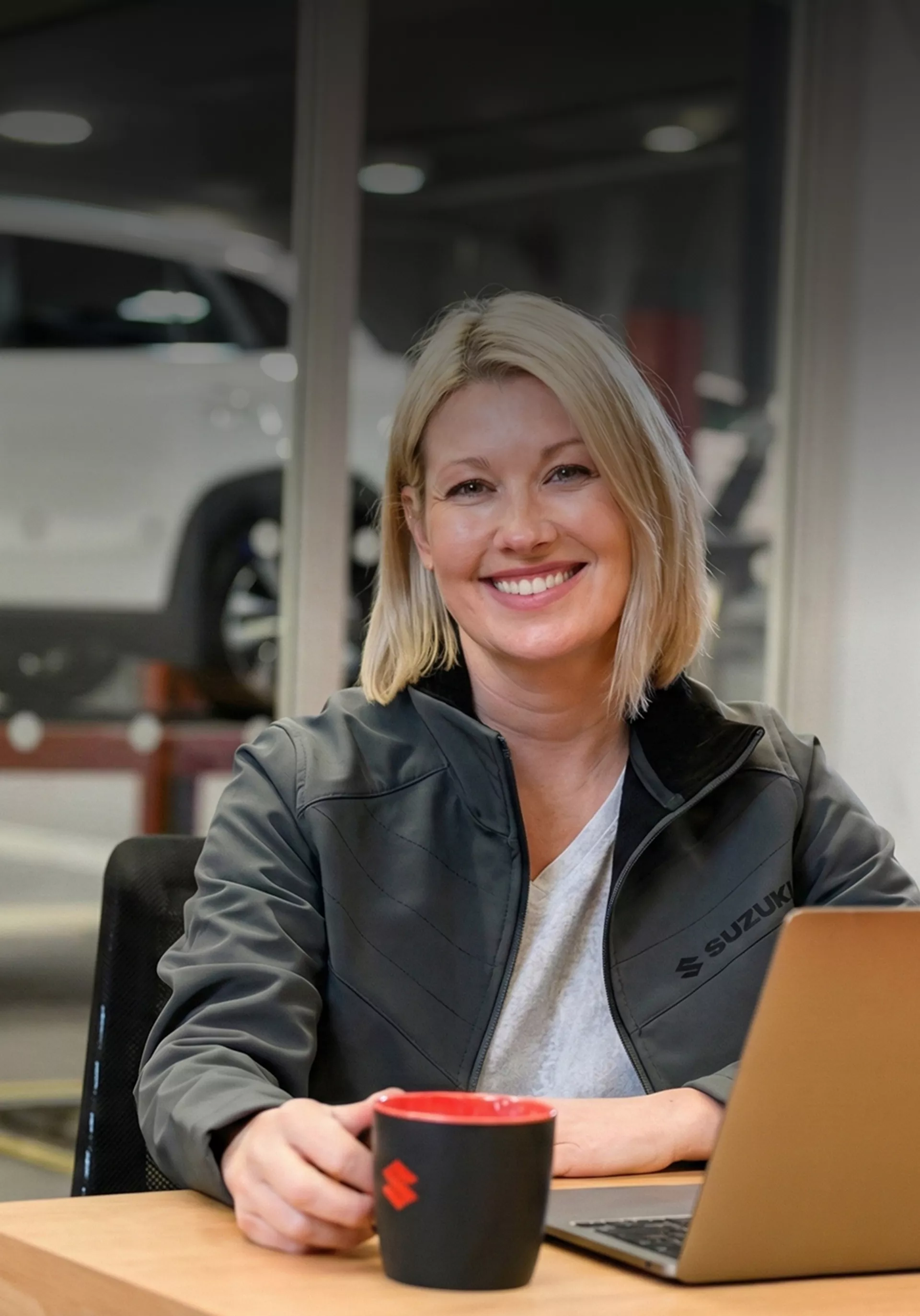 Suzuki employee sitting at a desk with a laptop inside a dealership showroom