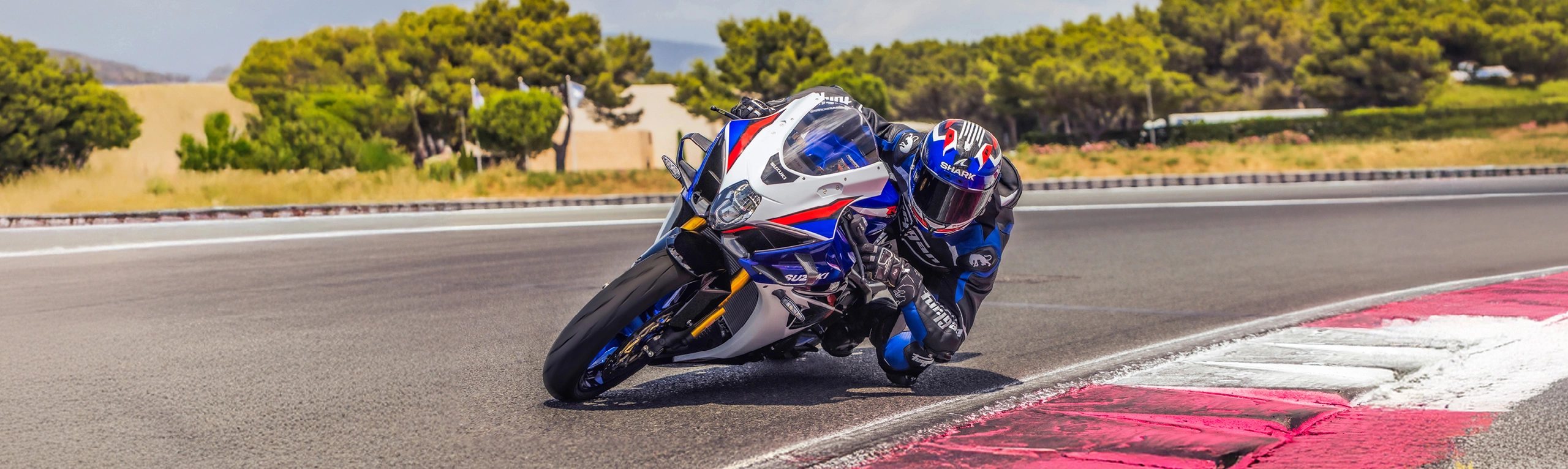 Suzuki GSX-R1000R blue, leaning hard into a corner, shot from in front of the bike inside the corner