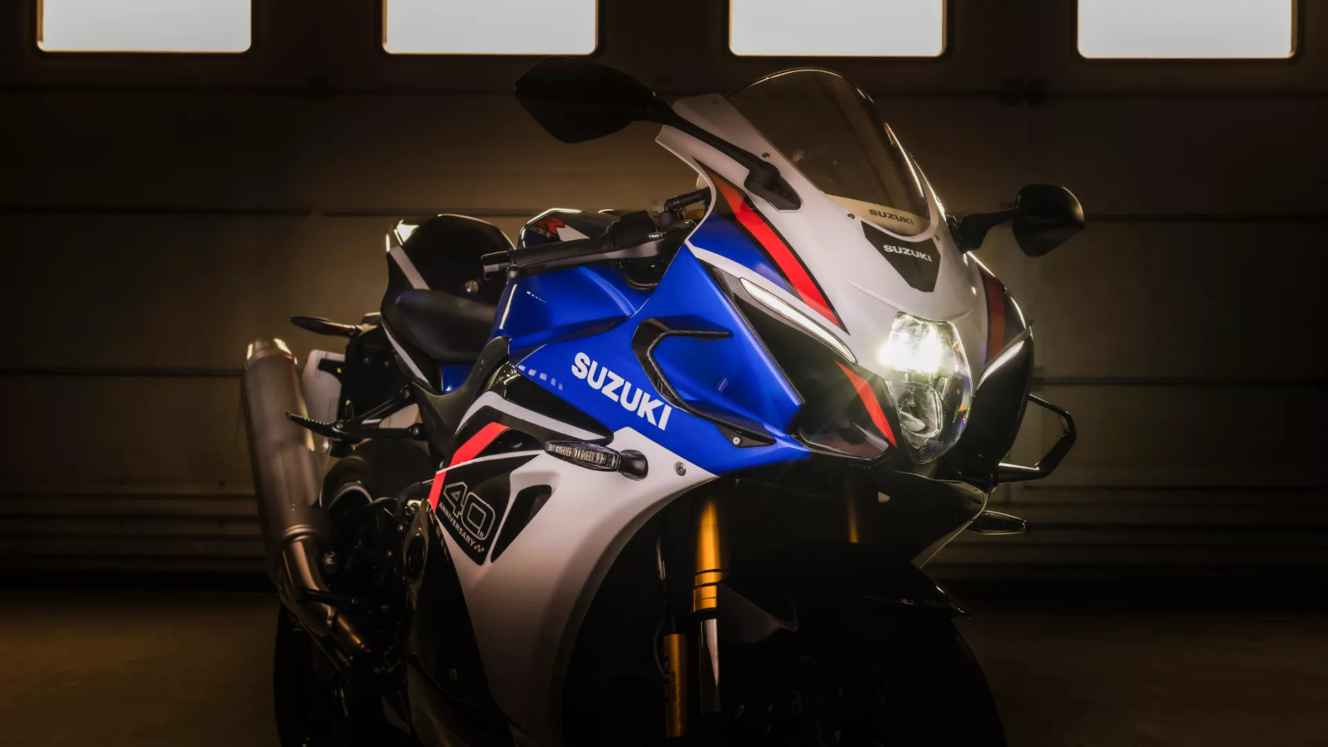 Suzuki GSX-R1000R front three quarter in a dark pit garage with headlight on
