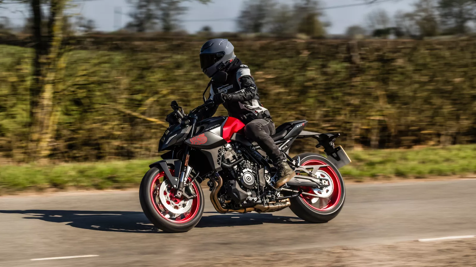 Suzuki GSX-8S red and black braking into a corner with trees and hedges behind.