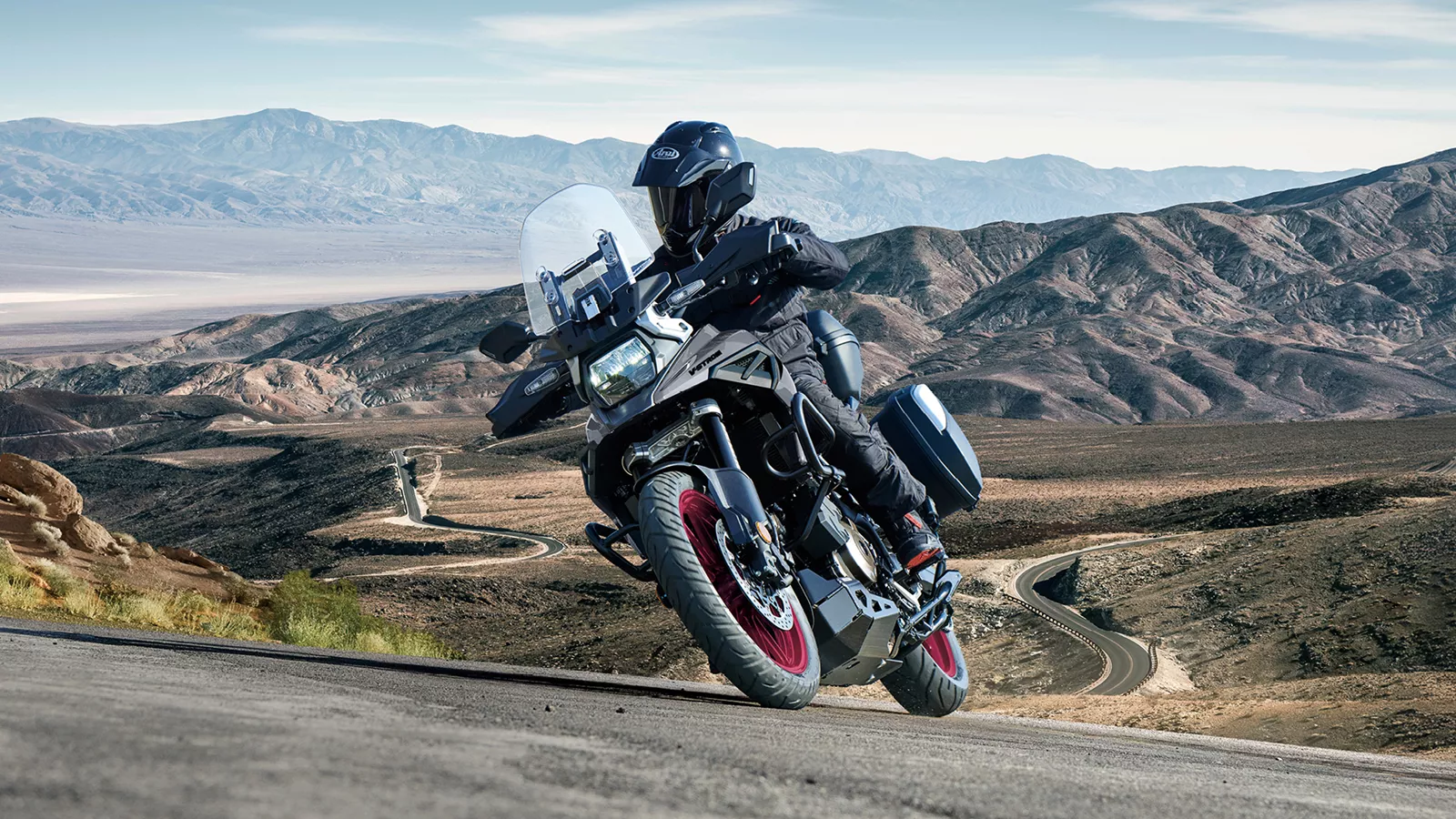 Suzuki V-Strom 1050RE grey pushing on through a corner with a mountain backdrop.