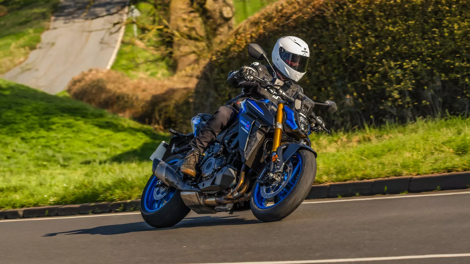 Suzuki GSX-S1000 blue pushing hard out of a corner on a country road