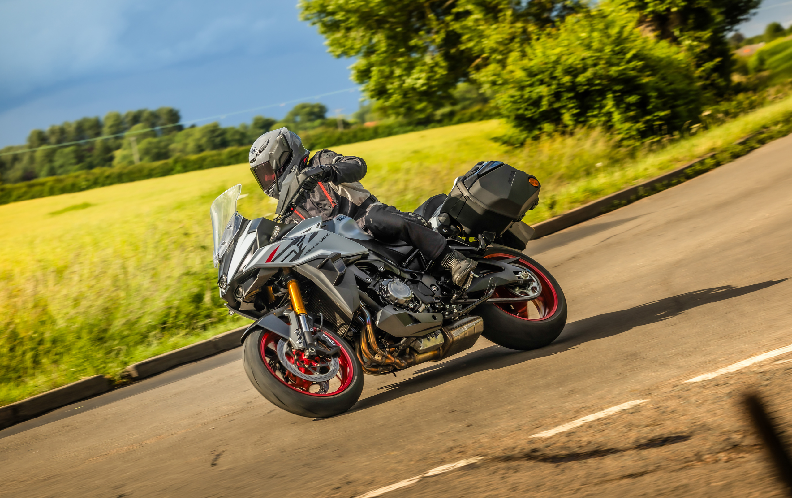 Suzuki GSX-S1000GX+ riding around a right hand bend with a field behind