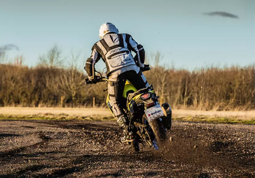 A rear view of the Suzuki V-Strom 800DE throwing up gravel on a dirt track, demonstrating its power and off-road performance.