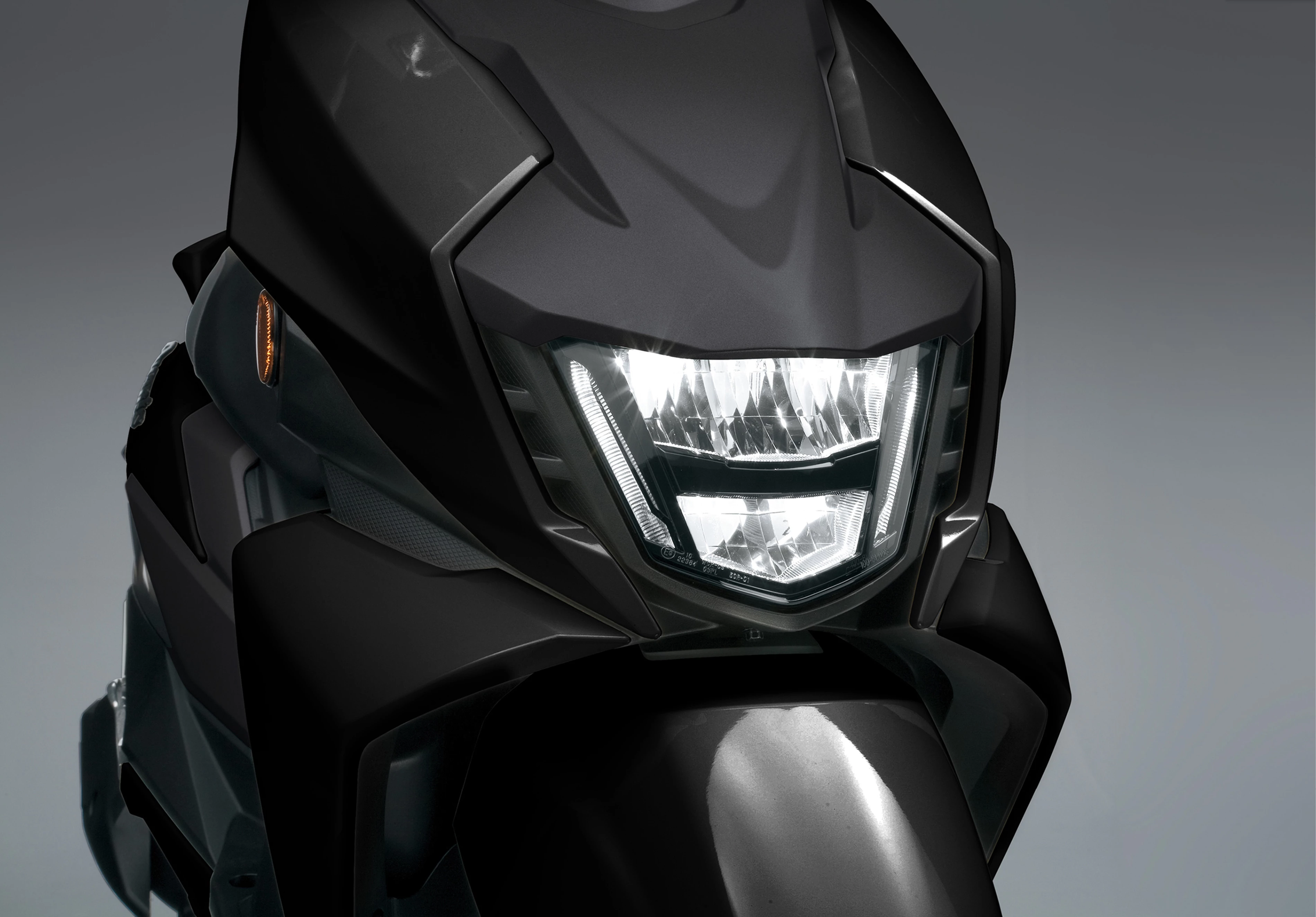 Suzuki Avenis 125 close-up of the headlight, highlighting its sharp design and bright illumination.