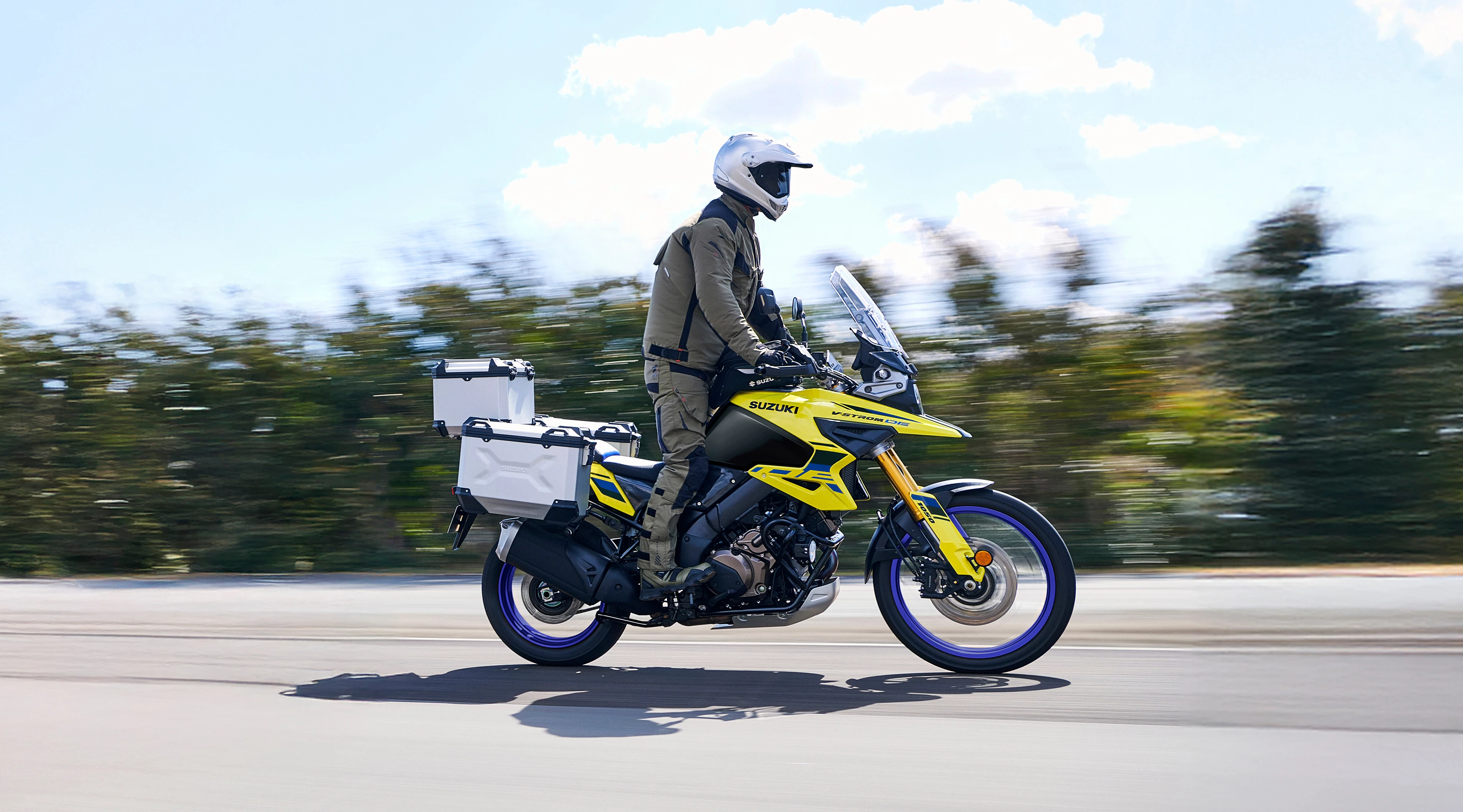 Suzuki V-Strom 1050DE Tour riding along a country road, with the rider up on the pegs