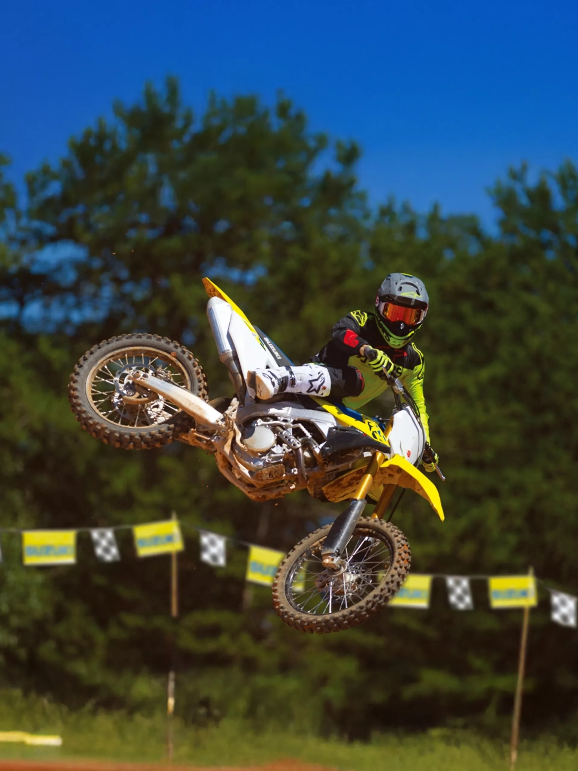 Suzuki RM-Z250 whip over a jump with trees in the background