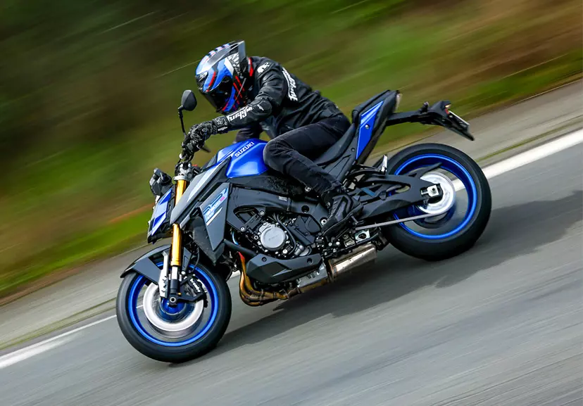 Suzuki GSX-S1000 leaning into a corner with a countryside background.