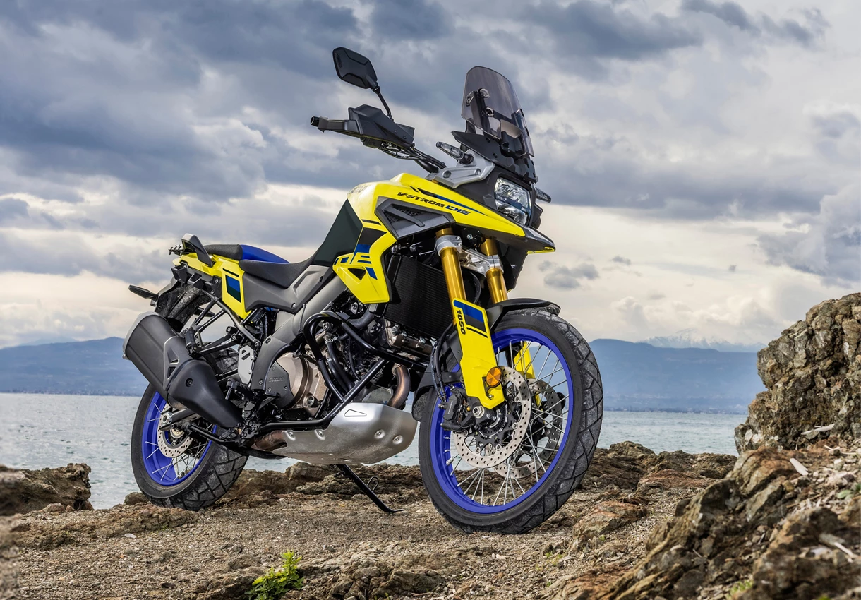 Suzuki V-Strom 1050DE front three quarters on a rocky outcrop next to the sea