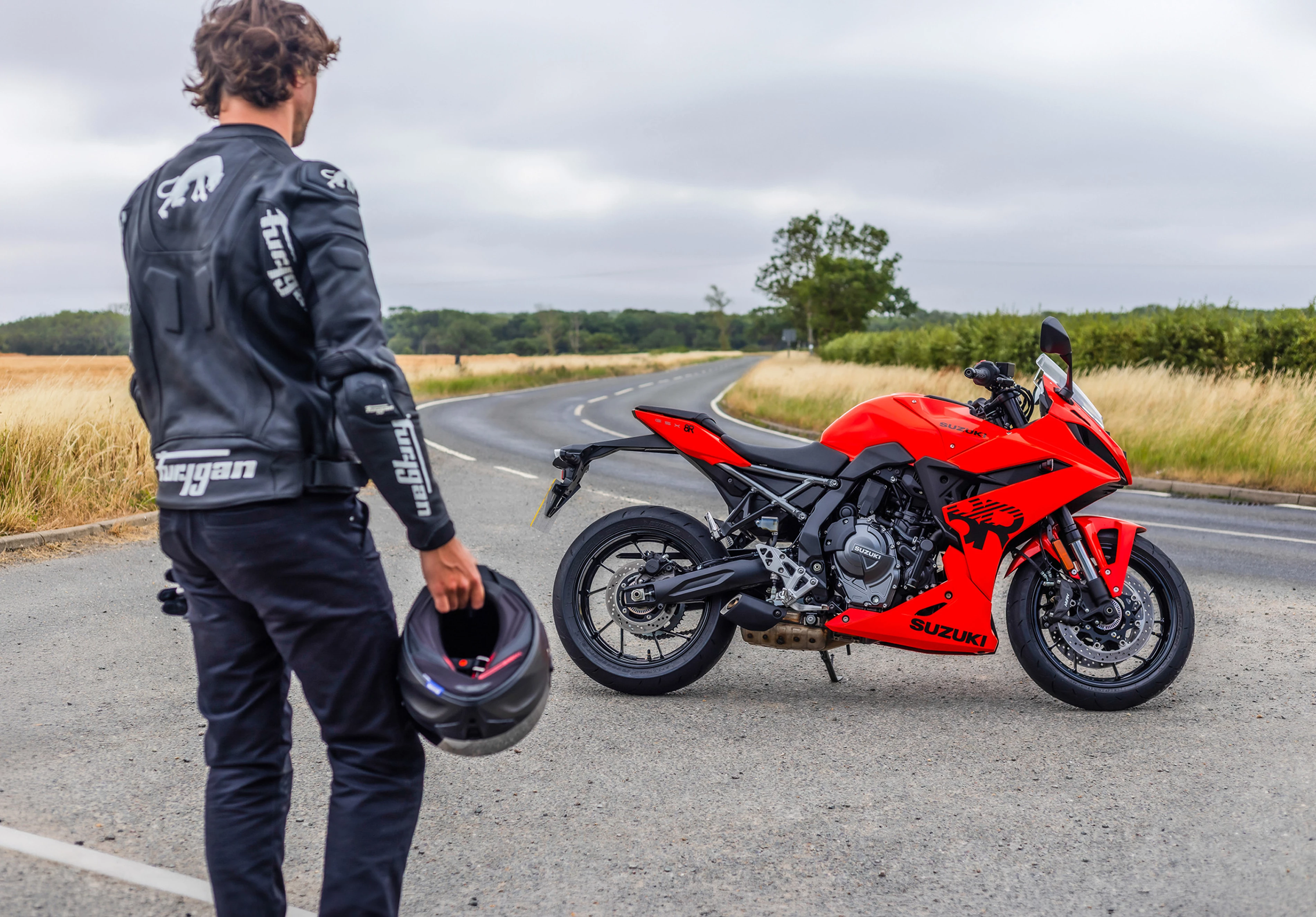 Suzuki GSX-8R static from the right hand side with a field in the background and a rider holding their helmet and gloves in the foreground
