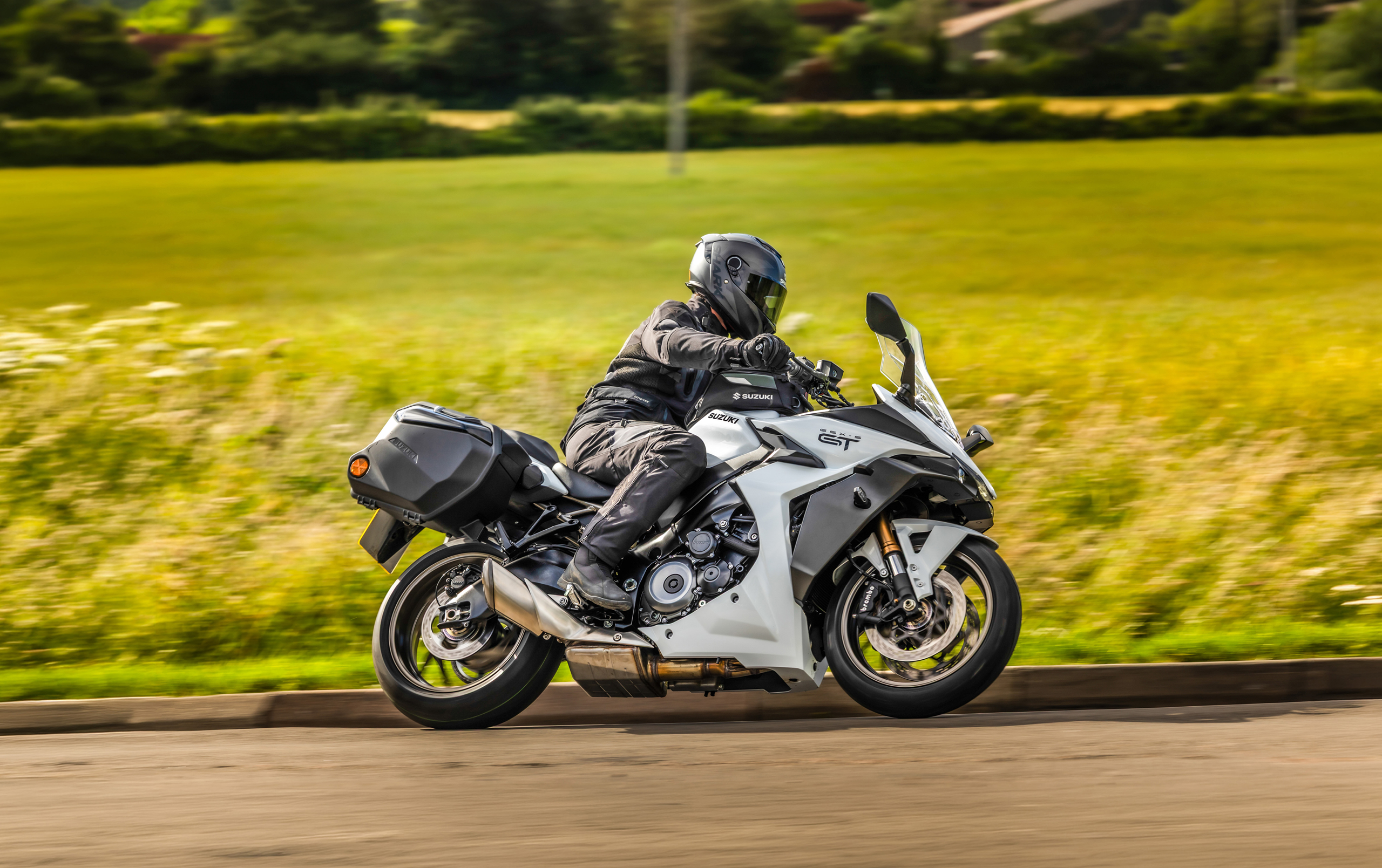 Suzuki GSX-S1000GT+ white leaning hard into a corner with a country field behind