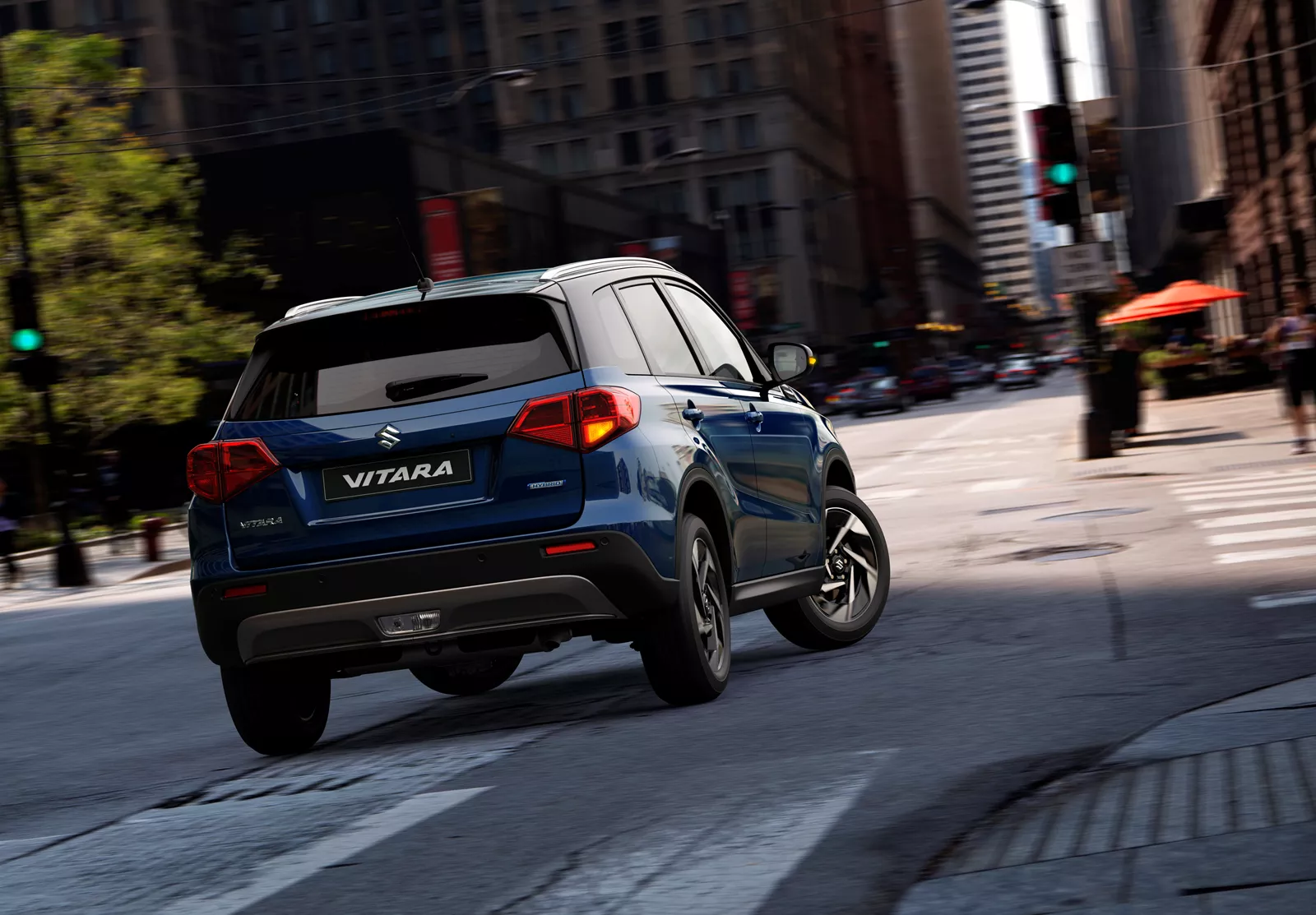 Rear view of the Suzuki Vitara in sphere blue driving through a city street, showcasing its urban styling and compact SUV design.