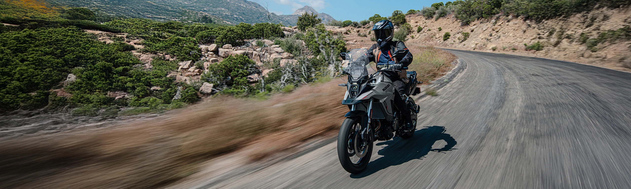 Suzuki V-Strom 800RE grey riding along a mountain road.
