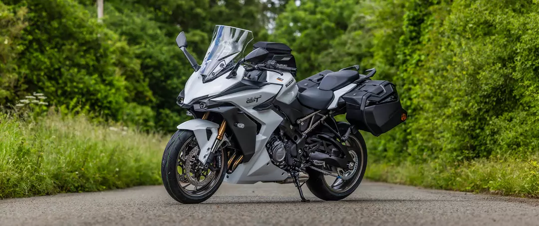 Suzuki GSX-S1000GT+ static left hand side front three quarter with tress and bushes in the background.