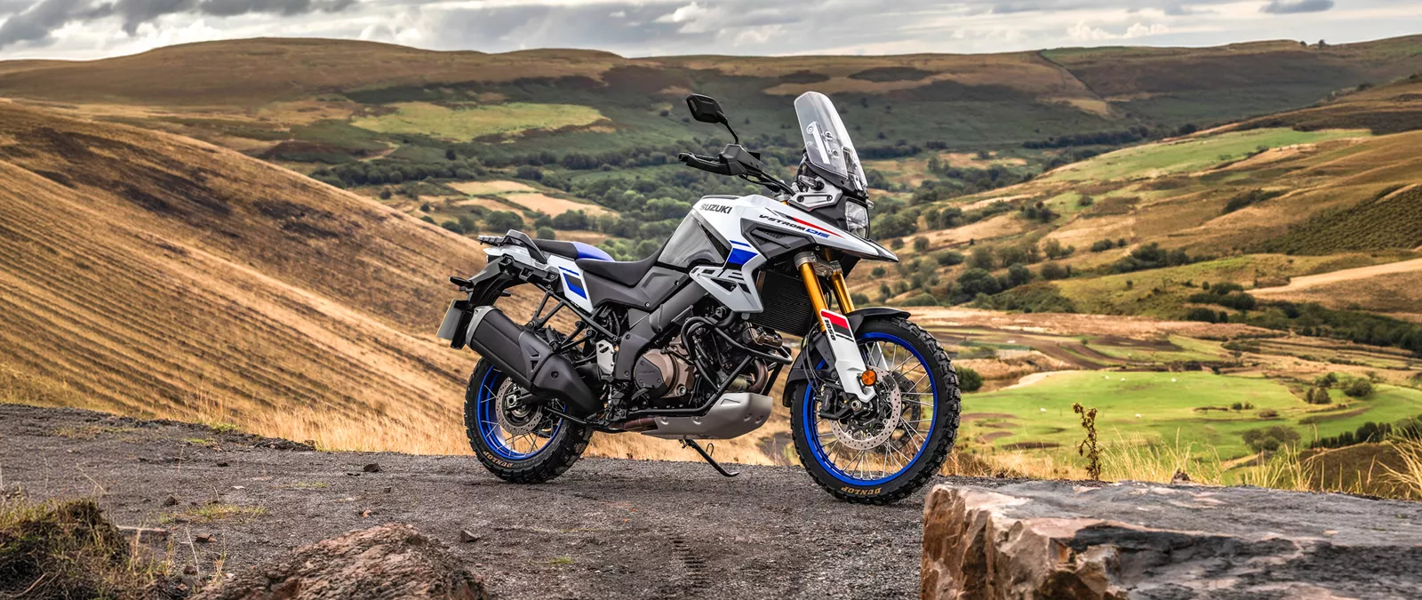 Suzuki V-Strom 1050DE white, on top of a hill with a valley behind