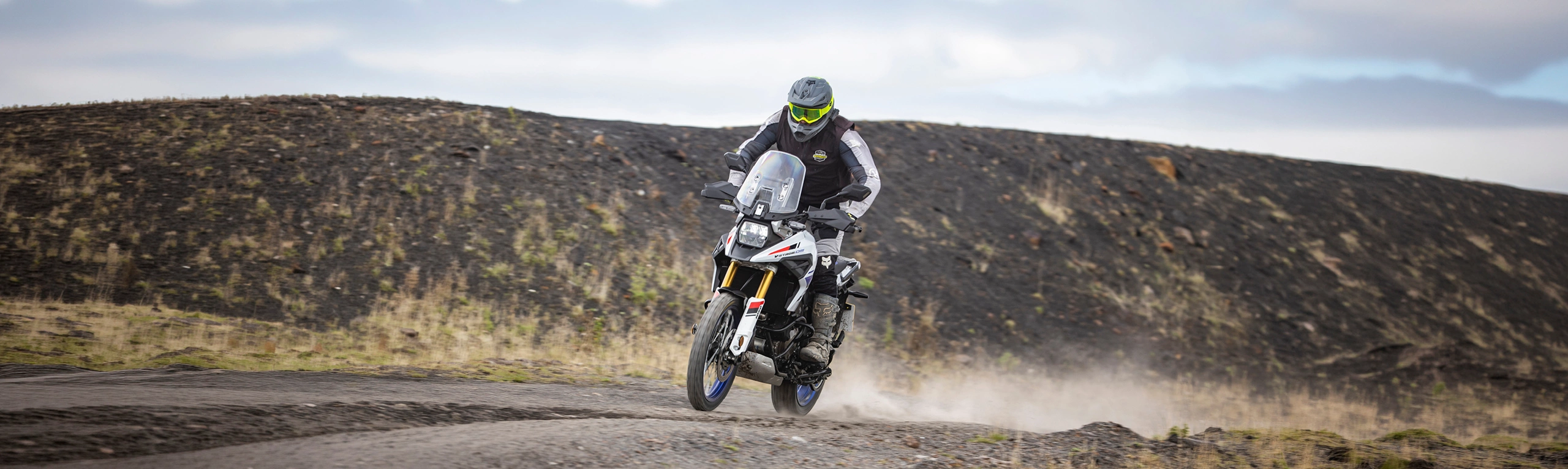 Suzuki V-Strom 1050DE white moving along a mountain trail at speed, with dust kicked up behind