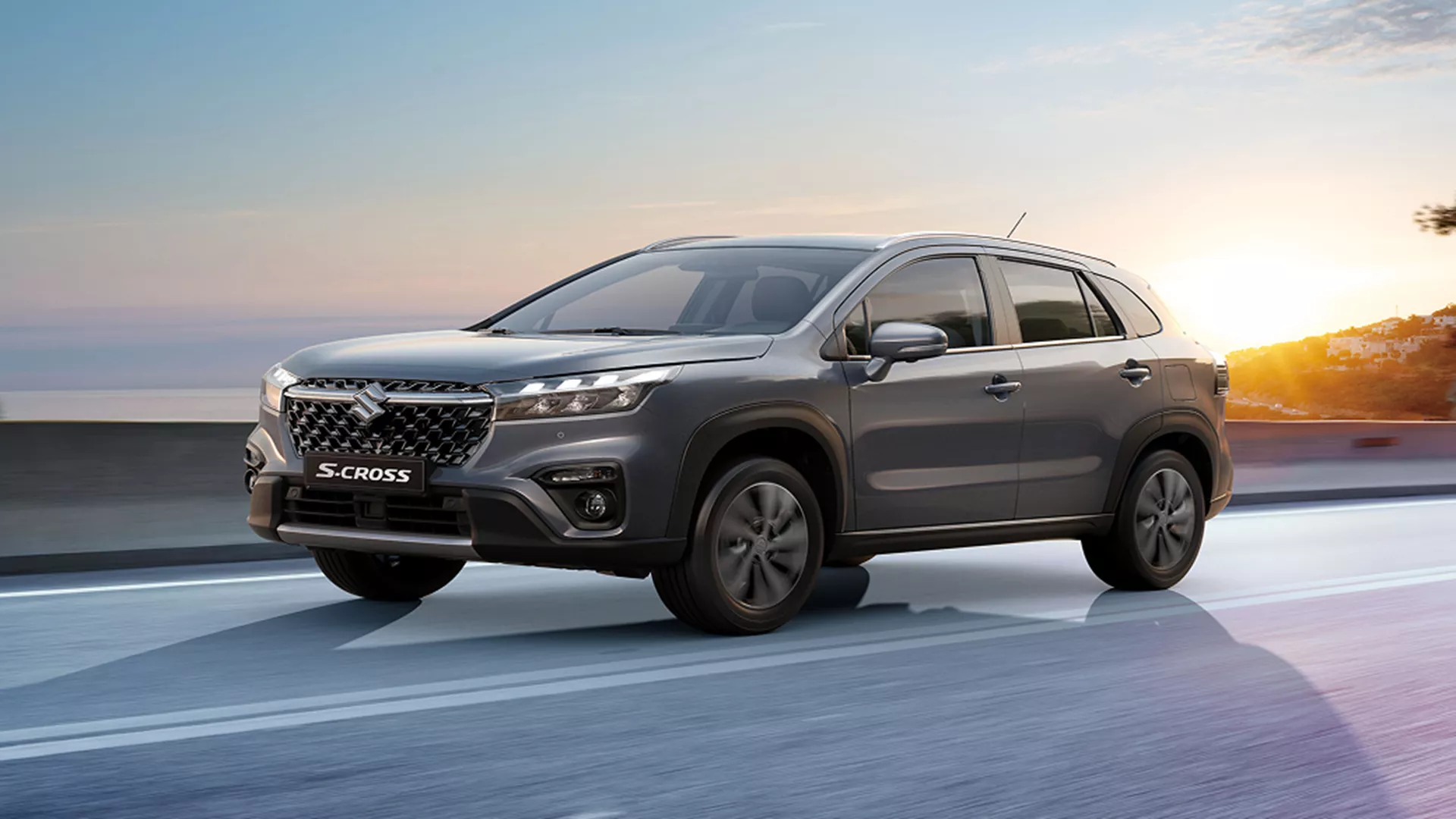 Grey Suzuki S-Cross driving on a coastal road at sunset