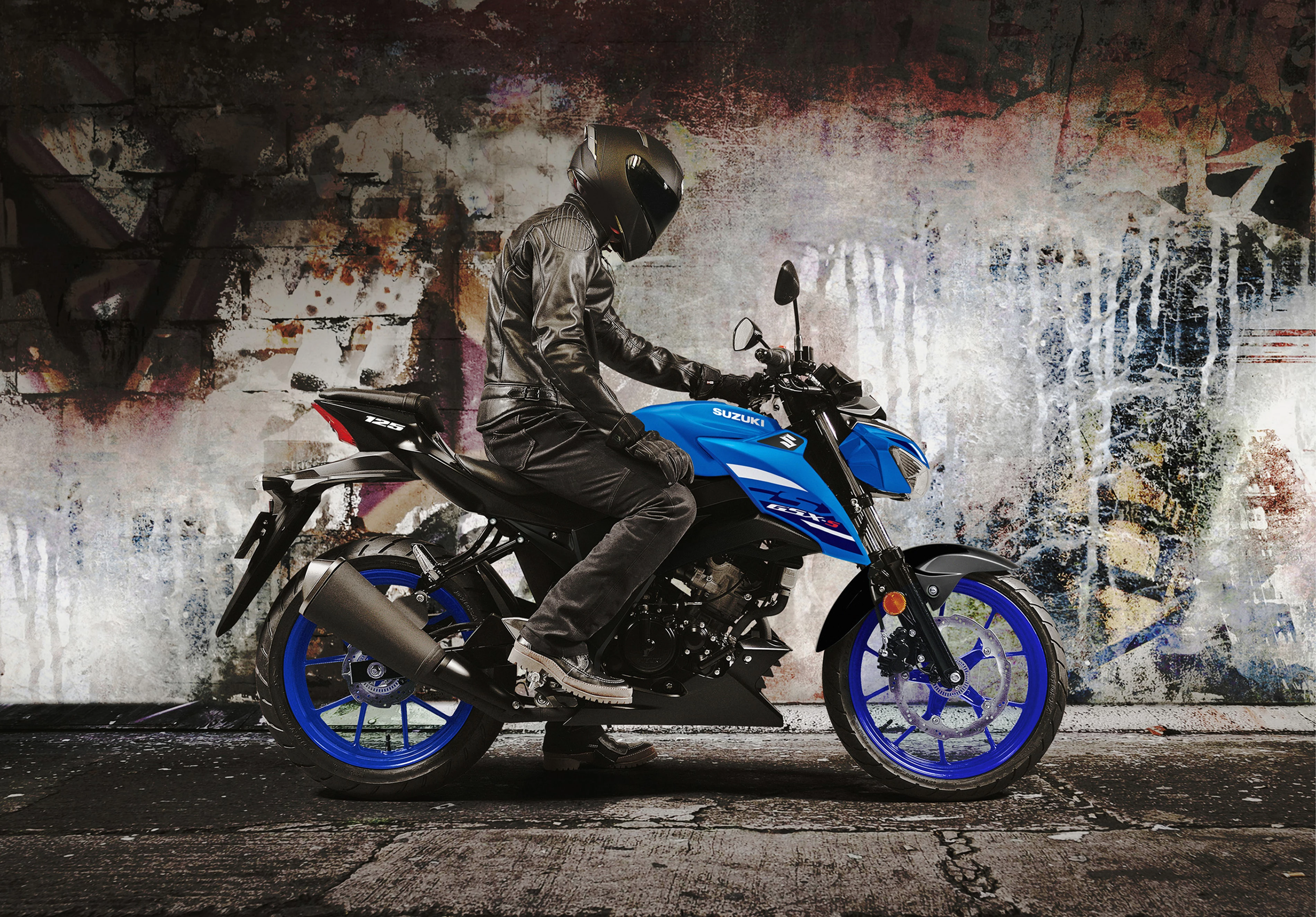 Suzuki GSX-S125 right hand side with a rider about to set off and a graffiti wall behind