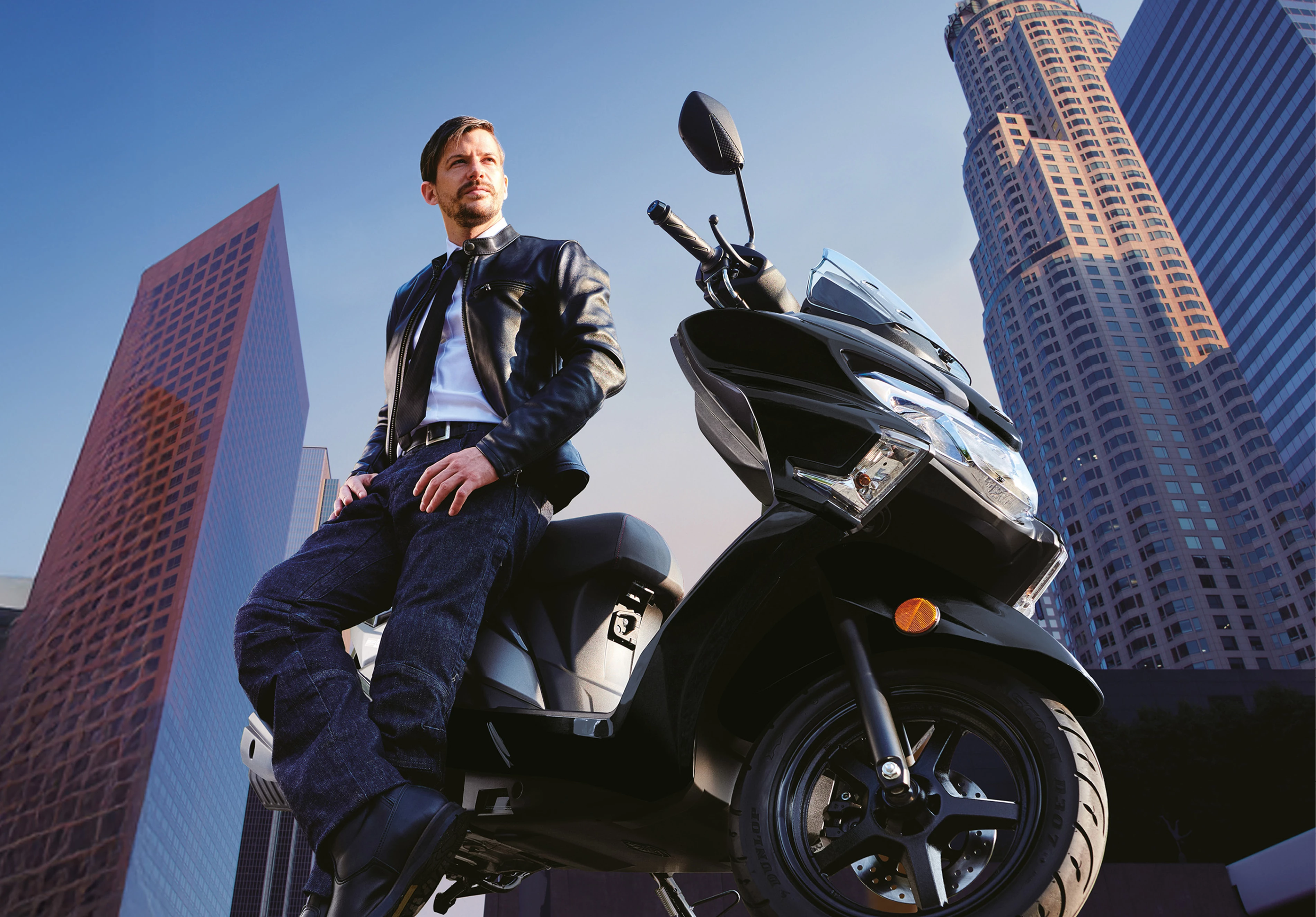 Suzuki Burgman Street 125EX rider in a black leather leaning on the bike with a city skycraper background