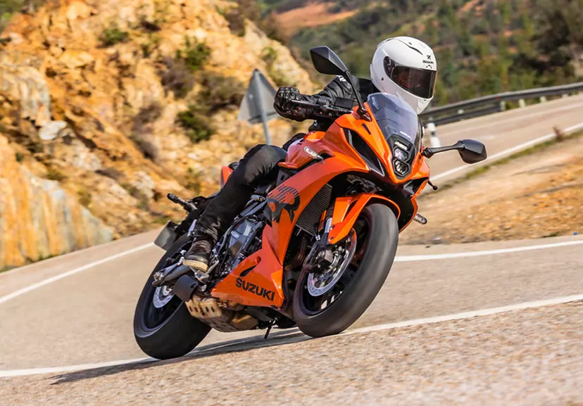 Suzuki GSX-8R leaning heavily into a corner with a sunny mountain road backdrop