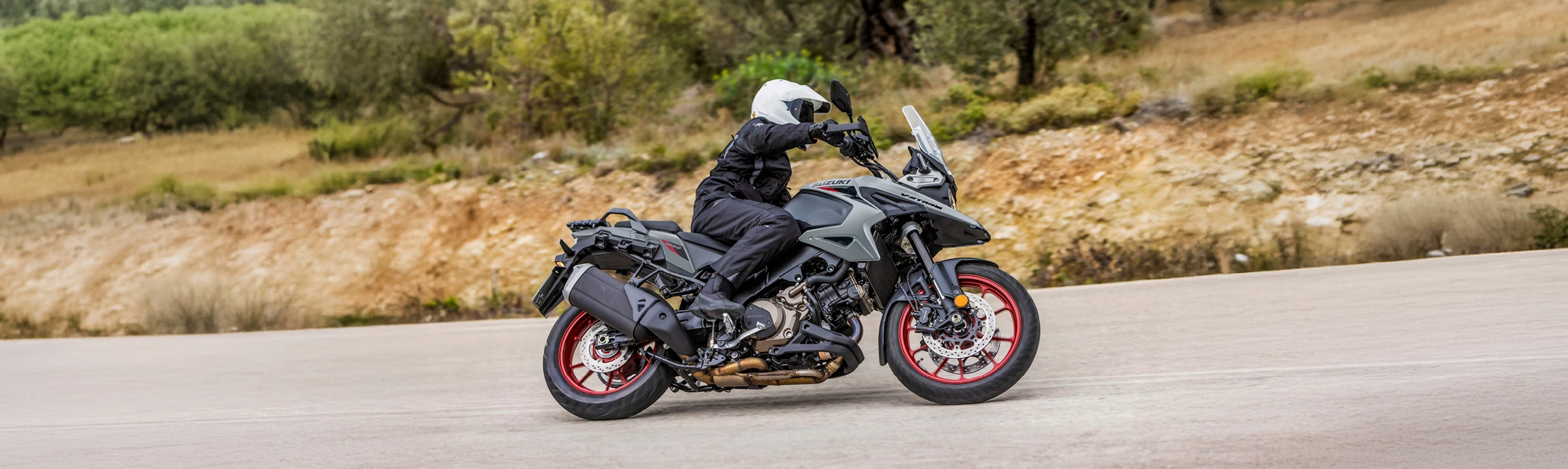 Suzuki V-Strom 1050RE grey pushing on through a corner with small trees behind