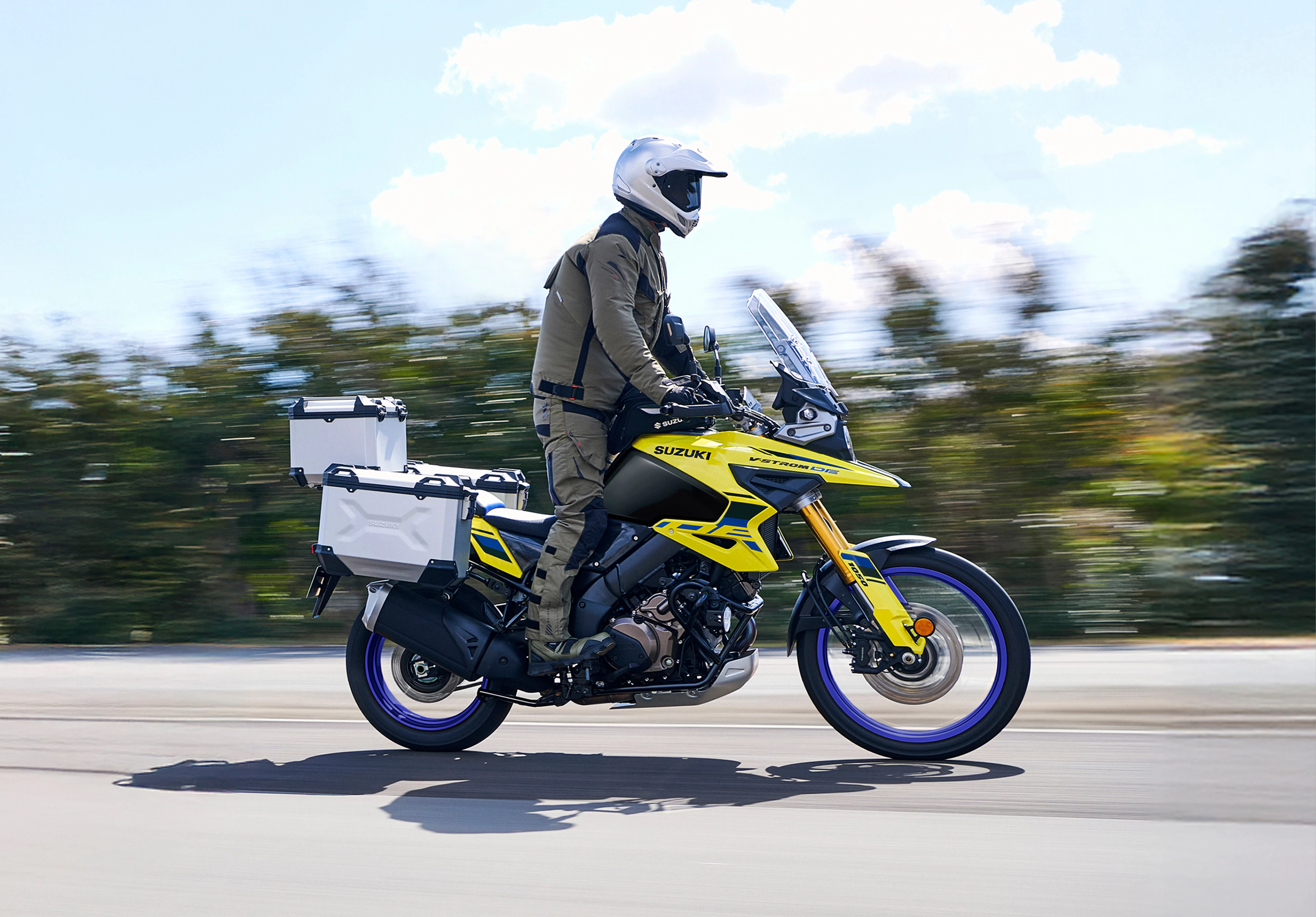 Suzuki V-Strom 1050DE Tour riding along a country road, with the rider up on the pegs