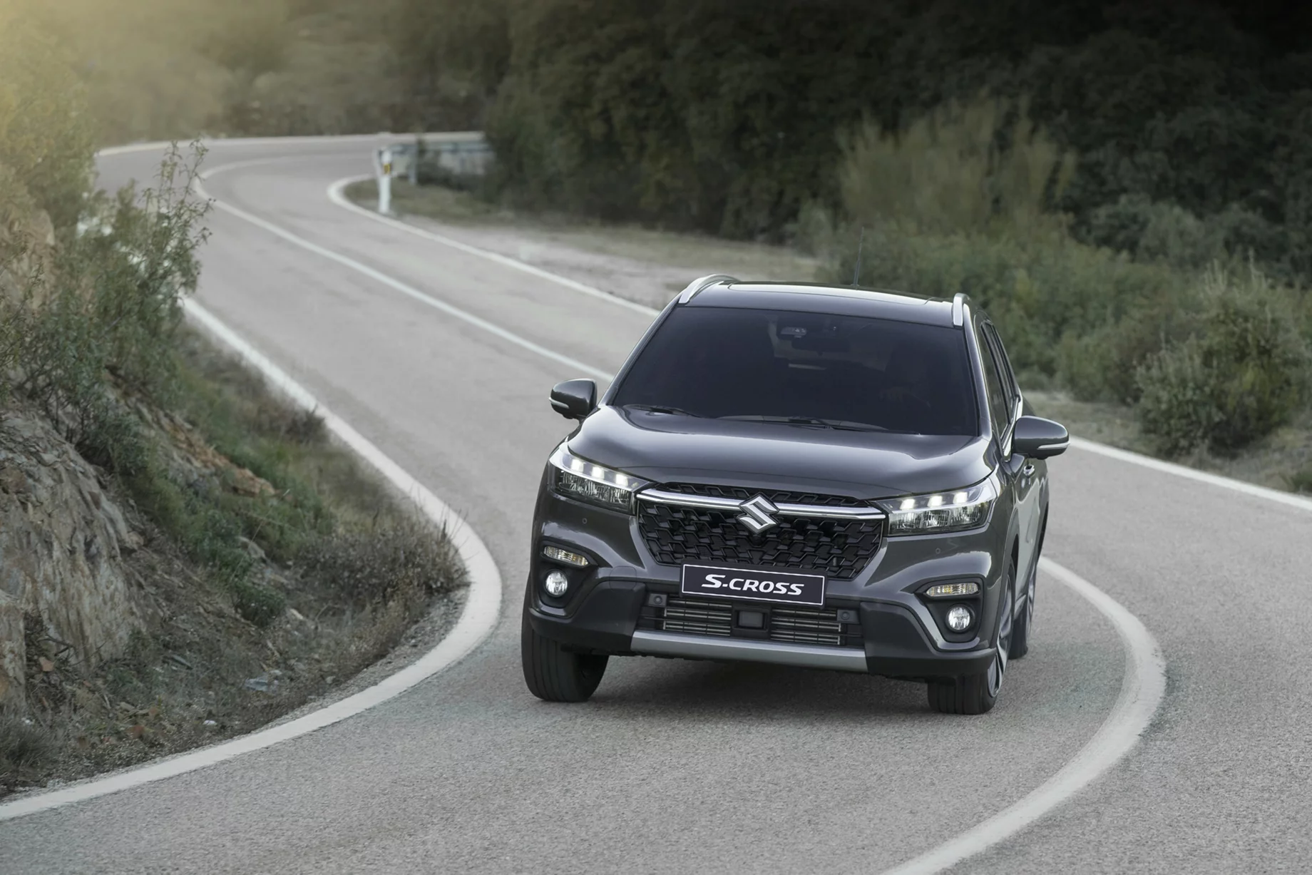 A Dark Grey Suzuki S-Cross driving on a winding country road.