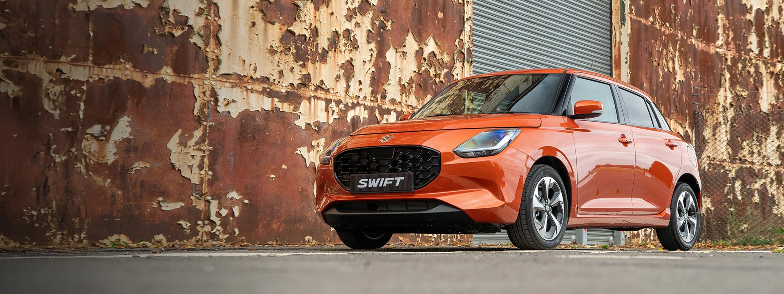 Flame Orange Suzuki Swift used car parked outside an industrial building