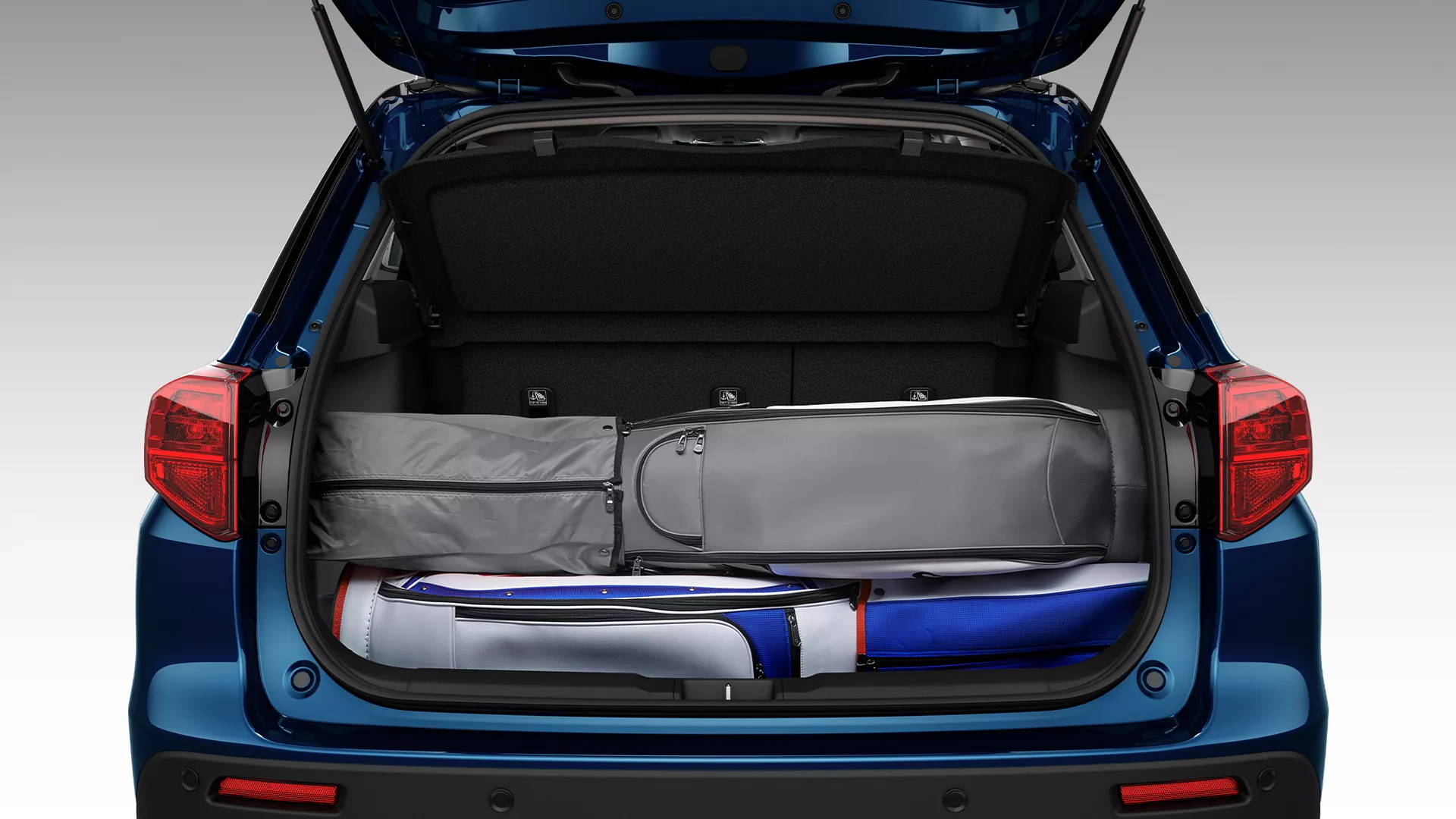 Open boot of the Suzuki Vitara showcasing an adjustable luggage floor with various travel bags neatly stored underneath for flexible storage configuration.