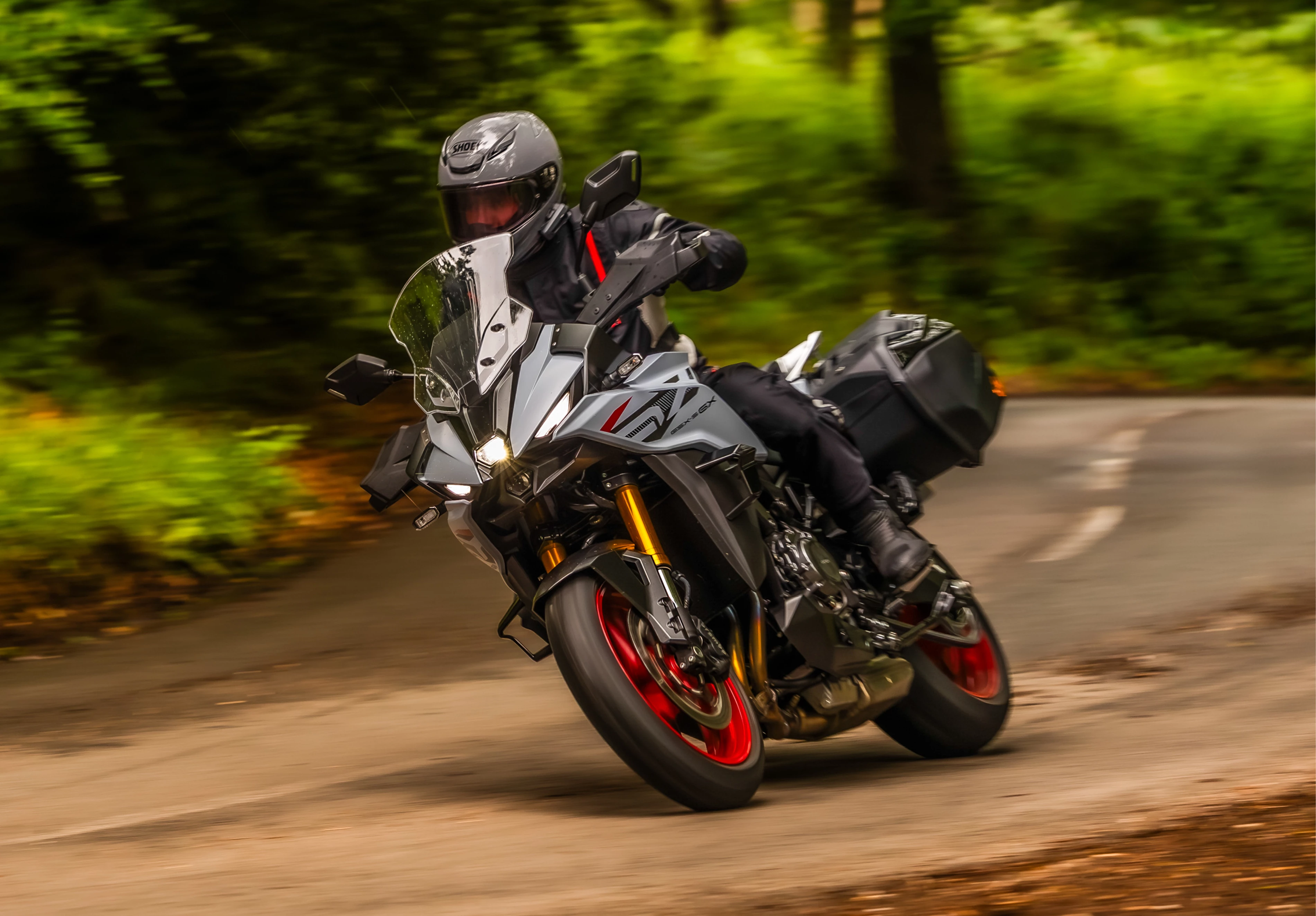 Suzuki GSX-S1000GX+ leaning into a corner of a forest lined road
