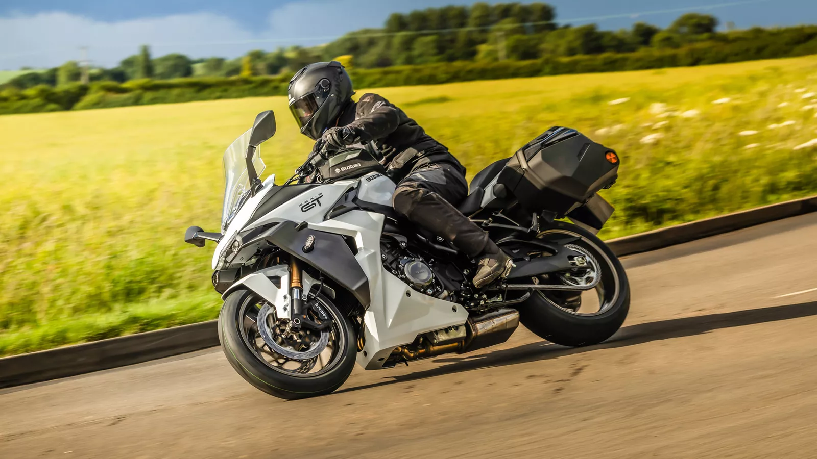 Suzuki GSX-S1000GT+ white leaning hard into a corner with a country field behind