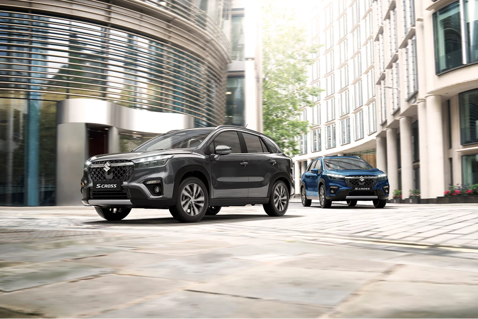 Grey Suzuki S-Cross Hybrid leading a blue S-Cross Hybrid in an urban setting